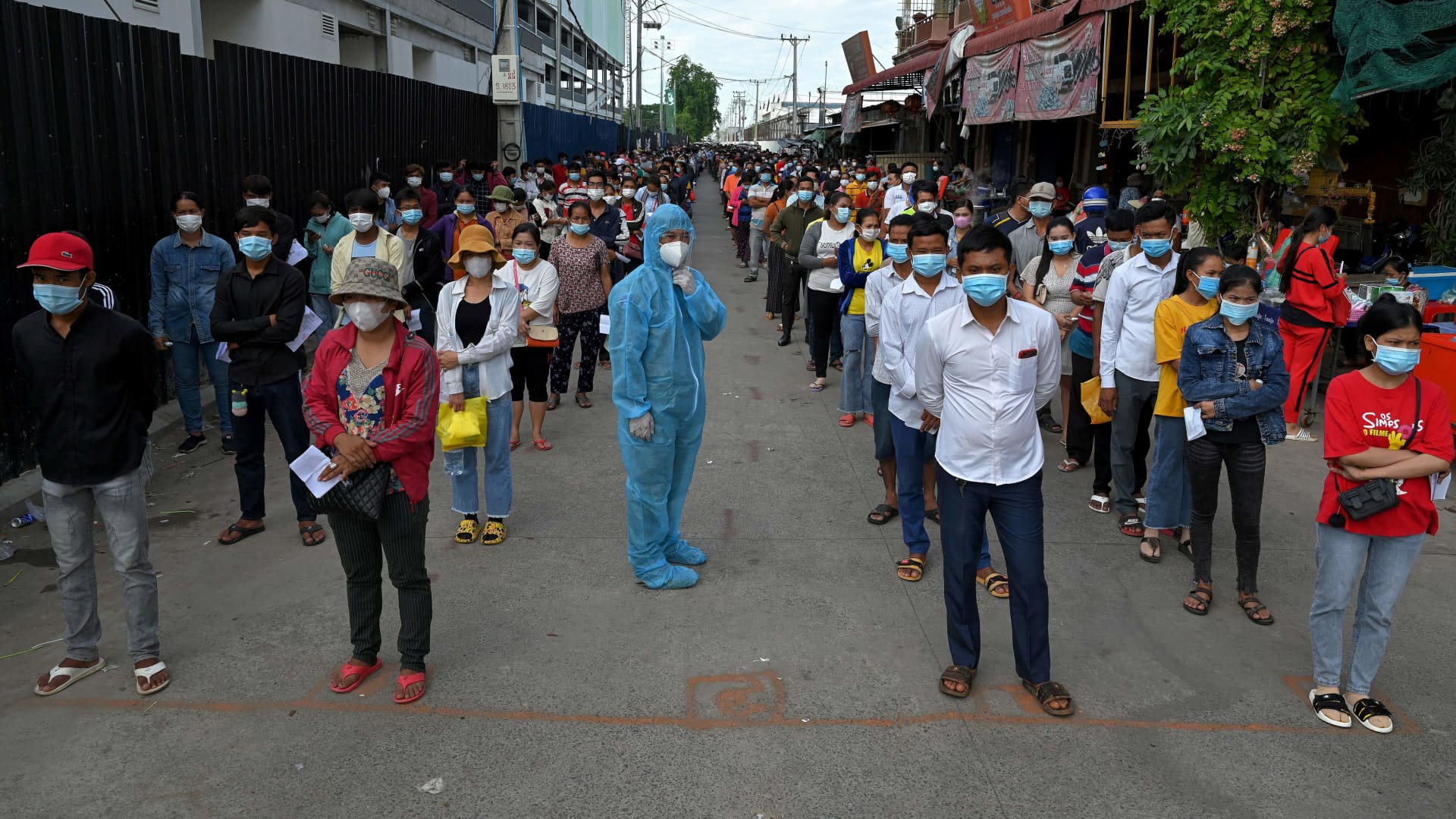 An official in personal protective equipment (PPE) manages the crowd as people queue to receive China's Sinopharm Covid-19 coronavirus vaccine in Phnom Penh on May 31, 2021, as part of the government's campaign to halt the rising number of cases of the virus.