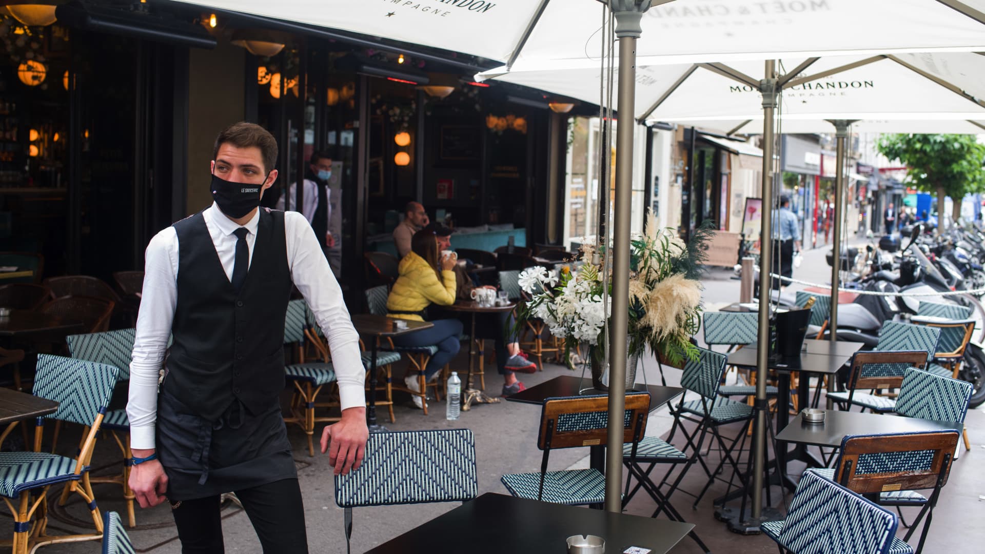 A waiter waits for customers on an extended cafe terrace area in Paris, France.