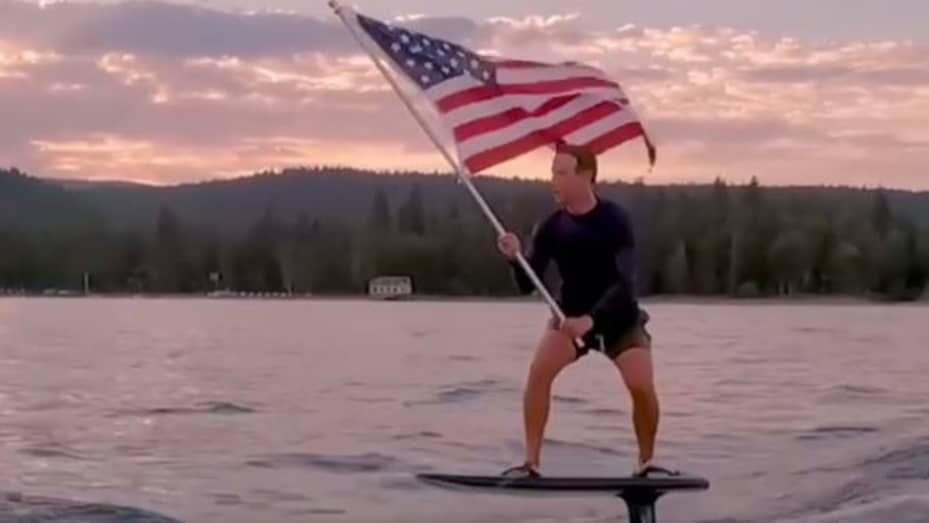 Facebook CEO Mark Zuckerberg rides a hydrofoil surfboard holding the American flag. July 4, 2021.