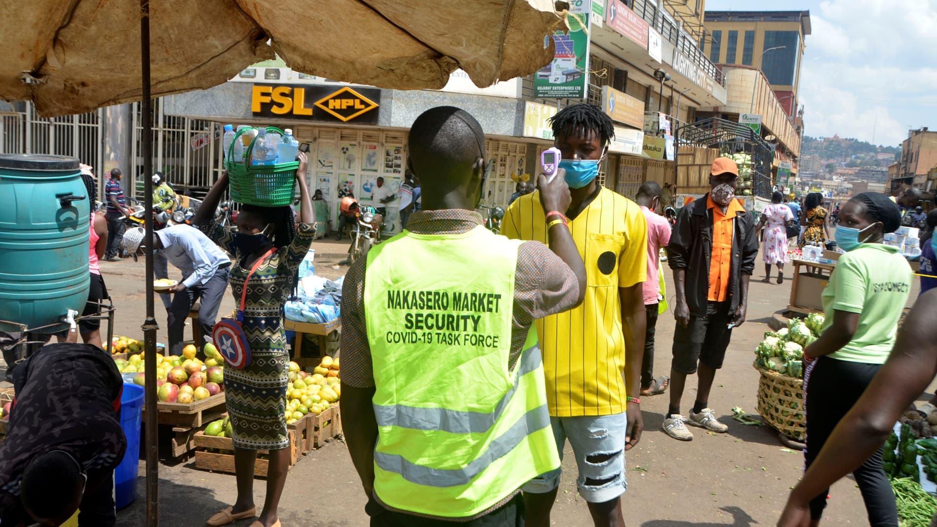 A security man measures a man's temperature at the entrance of a market in Kampala, Uganda, on June 20, 2021.