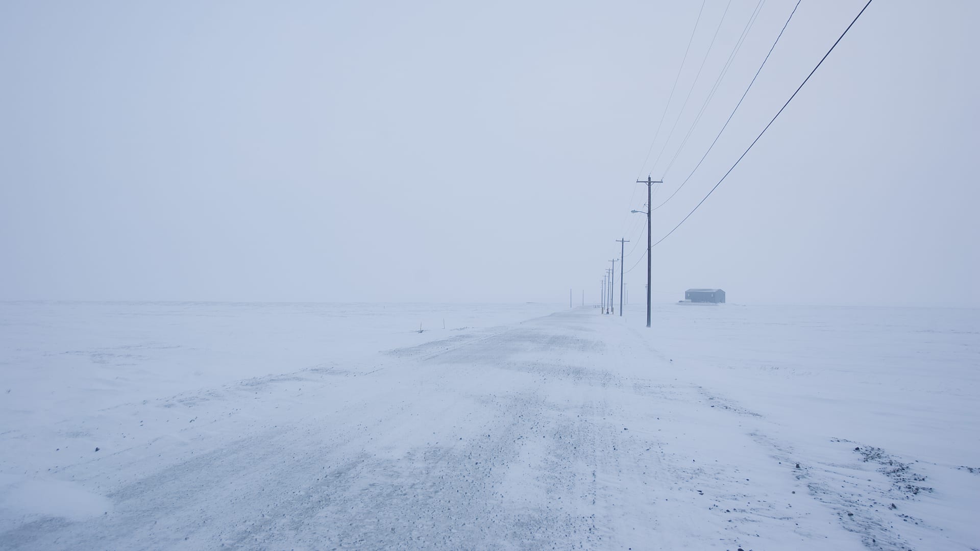 A snow covered road with power lines in Kaktovic, Alaska.