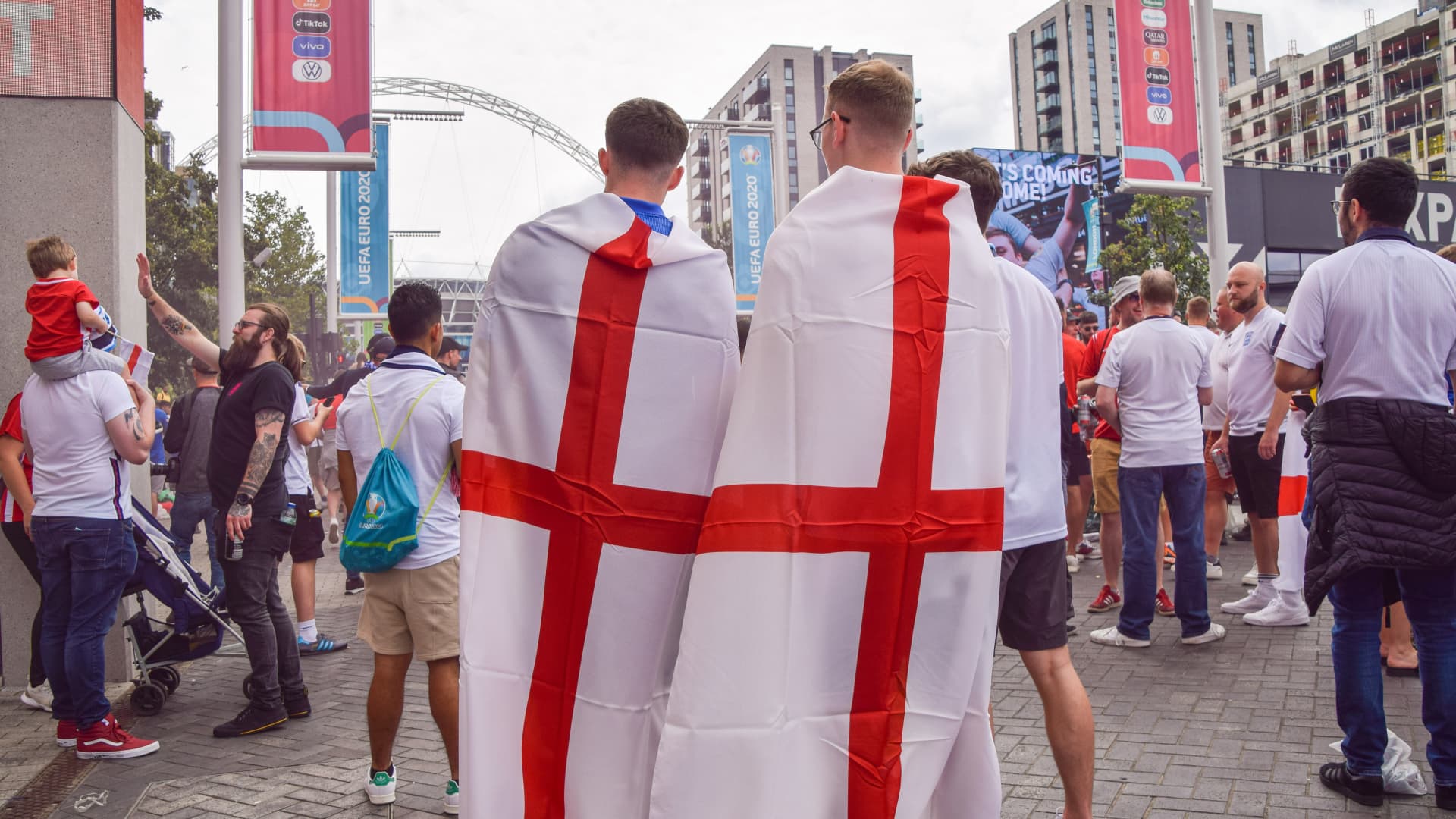 Football fans wrapped in English flags stand outside Wembley Stadium ahead of the England v Italy Euro 2020 final.