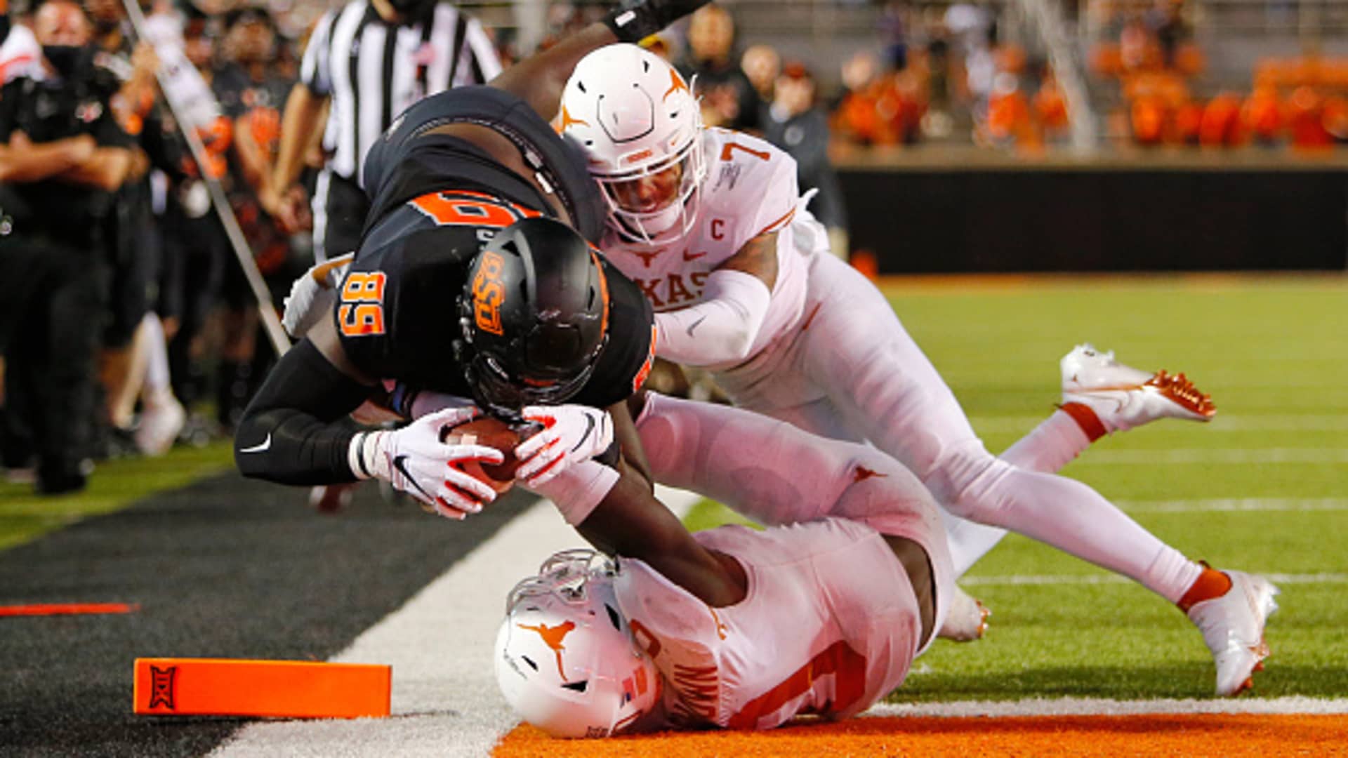 Tight end Jelani Woods #89 of the Oklahoma State Cowboys dives into the end zone for a nullified overtime touchdown against defensive back Caden Sterns #7 and linebacker DeMarvion Overshown #0 of the Texas Longhorns at Boone Pickens Stadium on October 31, 2020 in Stillwater, Oklahoma.
