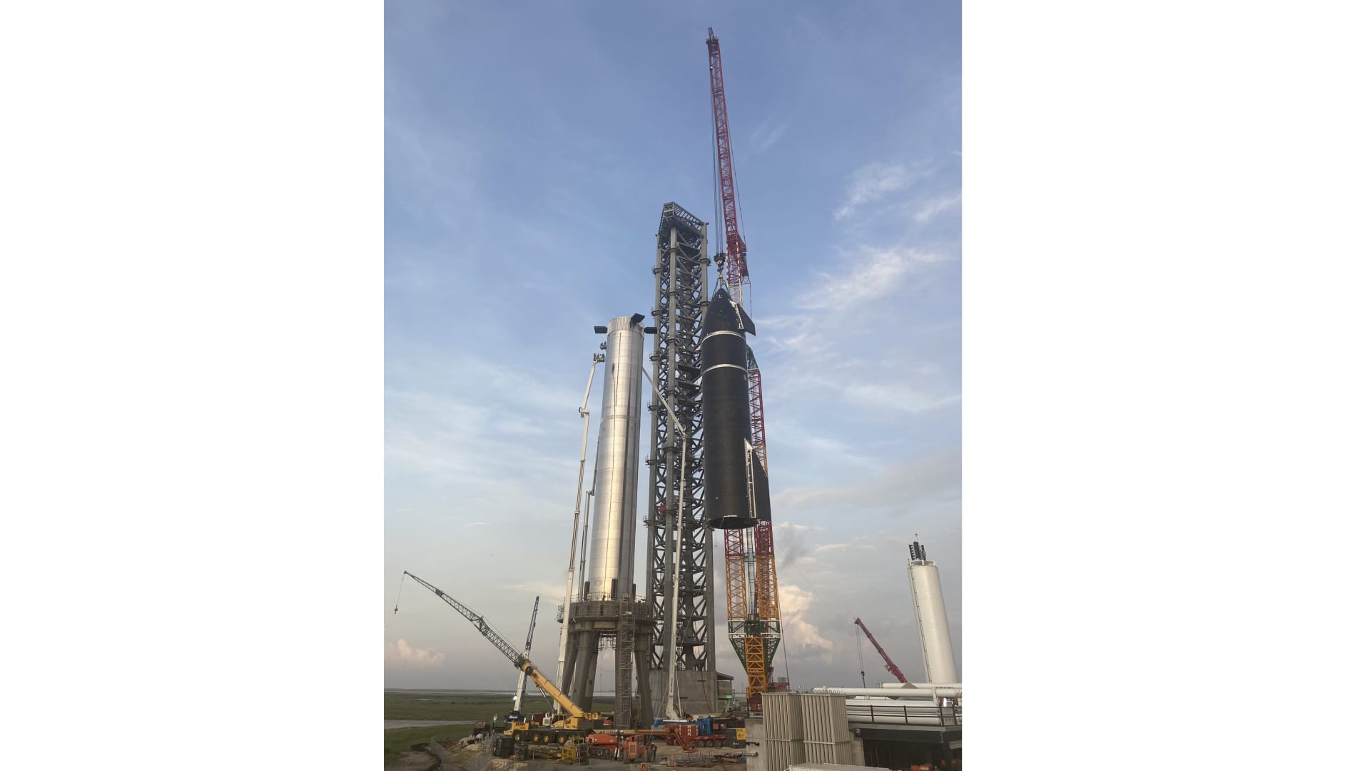 A SpaceX crane lifts Starship prototype 20 on top of Super Heavy rocket Booster 4 during stacking operations on August 6, 2021.