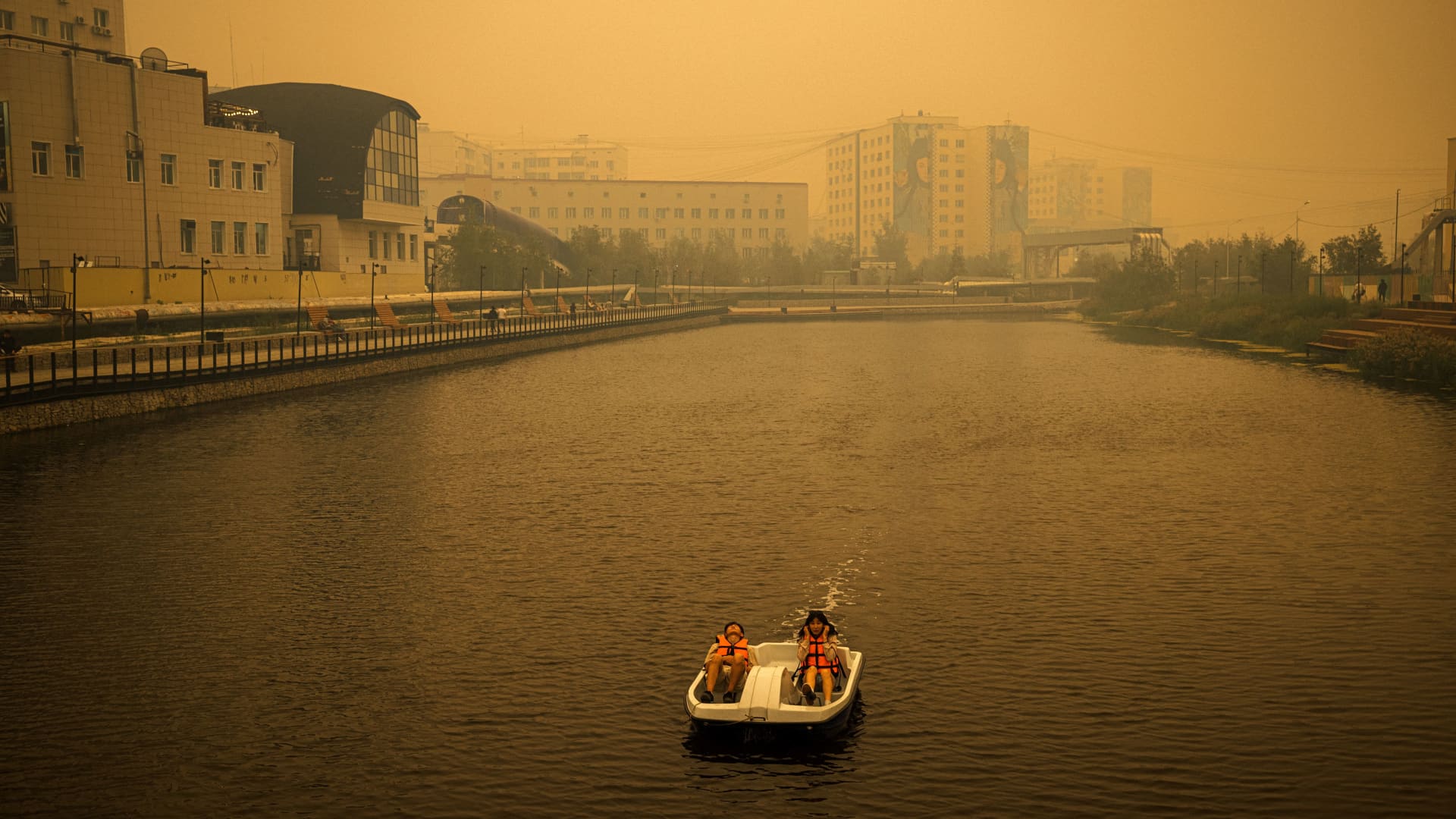 A couple rides a pedal boat as smoke from nearby forest fires hangs over the city of Yakutsk, in the republic of Sakha, Siberia, on July 27, 2021.
