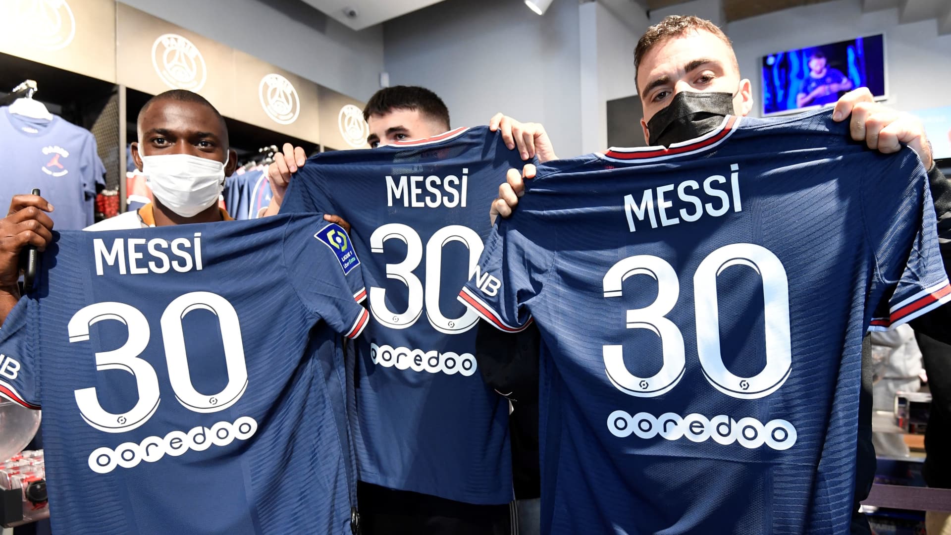 Supporters pose with jerseys of PSG's Argentinian football player Lionel Messi, that they have just bought at the Paris-Saint-Germain (PSG) football club store on the Champs Elysees avenue in Paris on August 11, 2021.