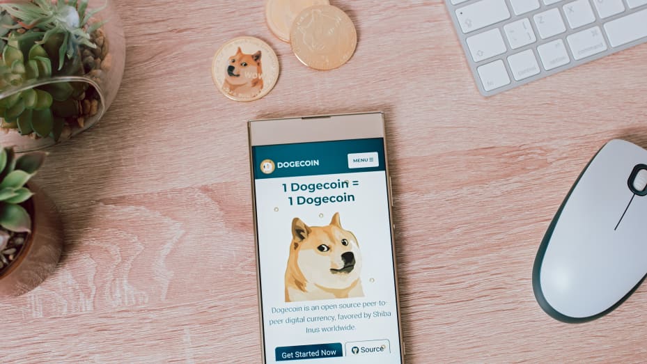 Dogecoin token and smartphone with Dogecoin website on background of work desk