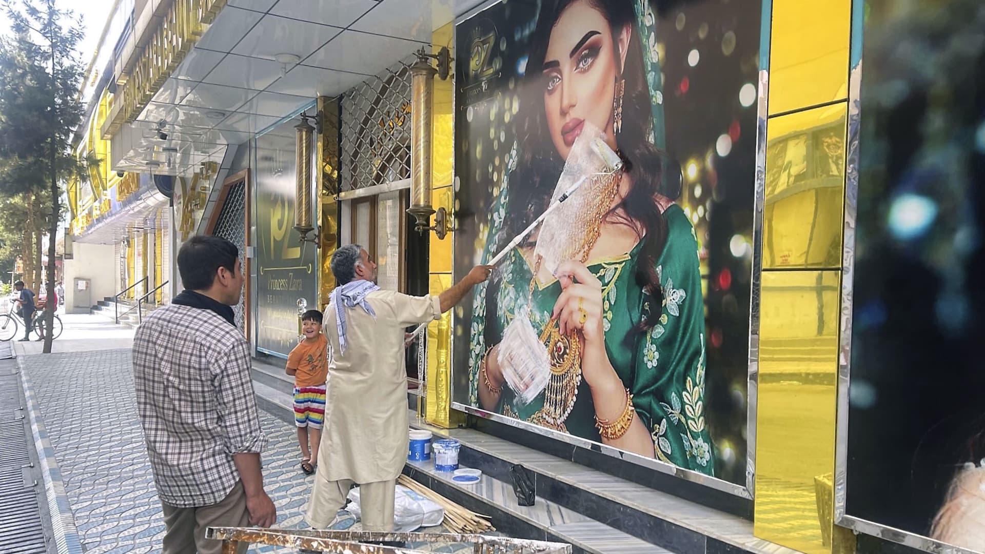 A worker at a beauty salon paints over a large photo of a woman on the wall in Kabul on Aug. 15, 2021, following news that the Taliban swept into the Afghan capital.