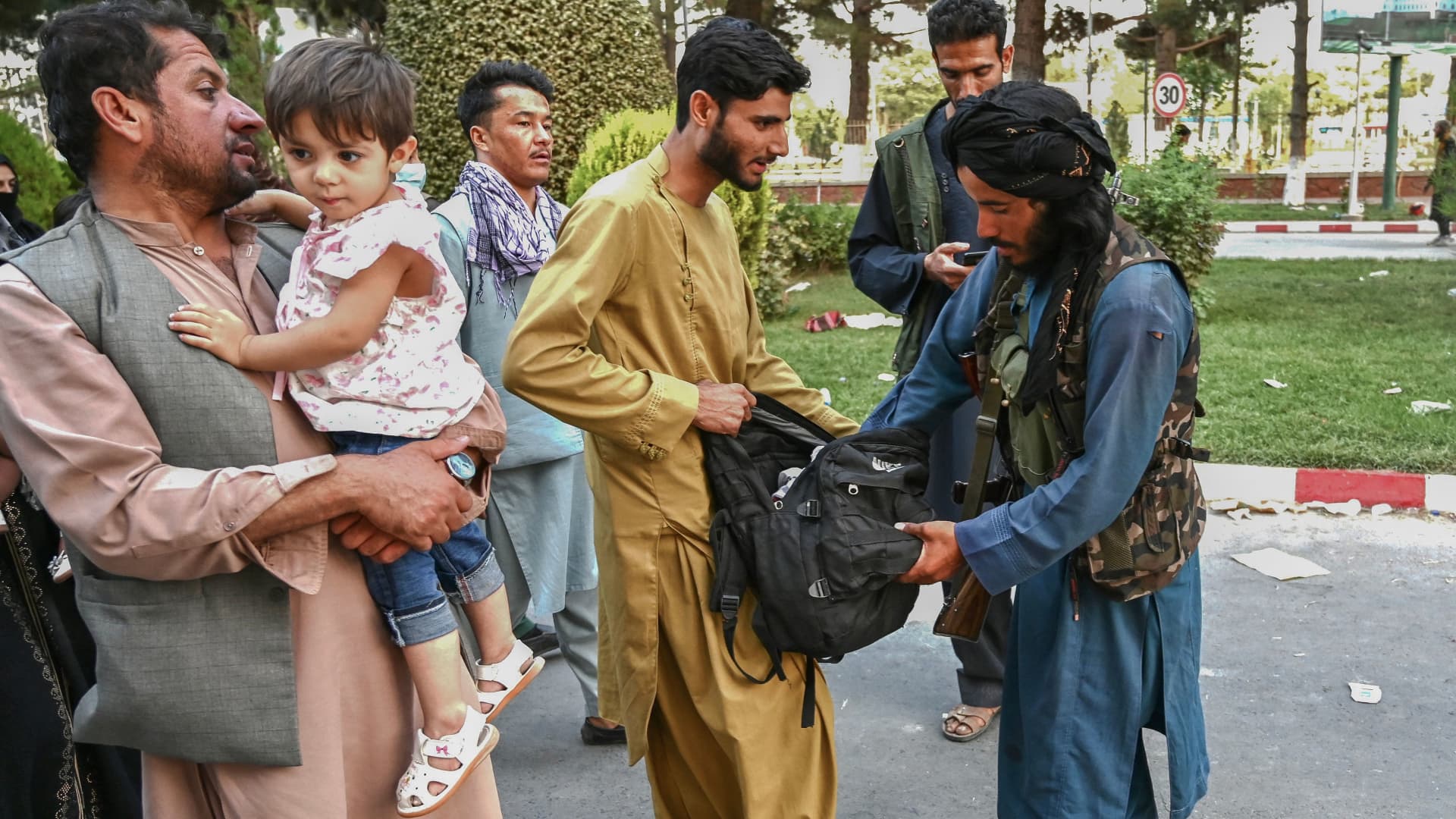 A Taliban fighter (R) searches the bags of people coming out of the Kabul airport in Kabul on August 16, 2021, after a stunningly swift end to Afghanistan's 20-year war, as thousands of people mobbed the city's airport trying to flee the group's feared hardline brand of Islamist rule.