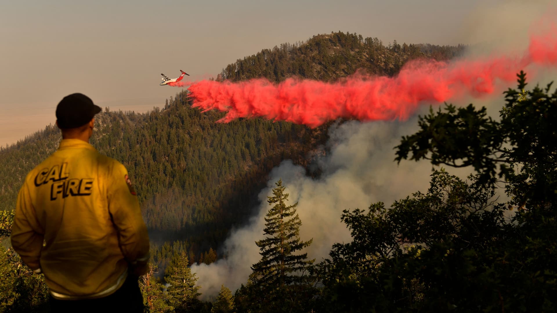 A Cal Fire firefighter from the Lassen-Modoc Unit watches as an air tanker makes a fire retardant drop on the Dixie Fire as trees burn on a hillside on August 18, 2021 near Janesville, California.