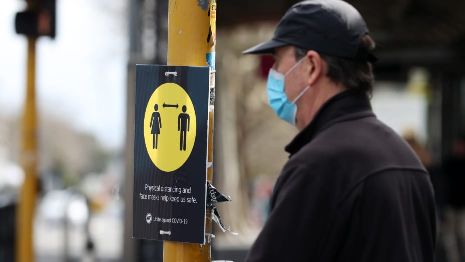 Personas con máscaras pasan por un letrero de distanciamiento físico en Ponsonby Rd ​​el 24 de agosto de 2021 en Auckland, Nueva Zelanda.  Las restricciones de bloqueo de nivel 4 están vigentes en toda Nueva Zelanda a medida que se continúan registrando nuevos casos de COVID-19.