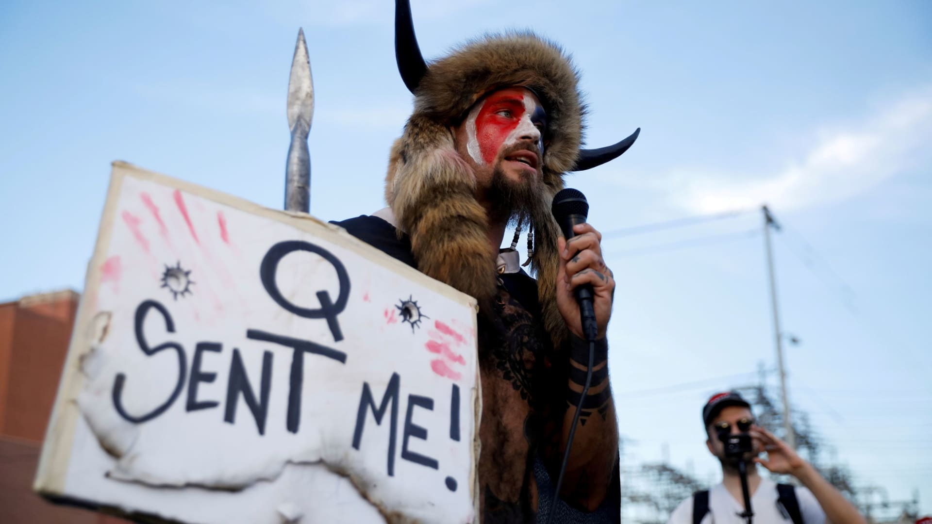 Jacob Chansley, holding a sign referencing QAnon, speaks as supporters of U.S. President Donald Trump gather to protest about the early results of the 2020 presidential election, in front of the Maricopa County Tabulation and Election Center (MCTEC), in Phoenix, Arizona November 5, 2020.