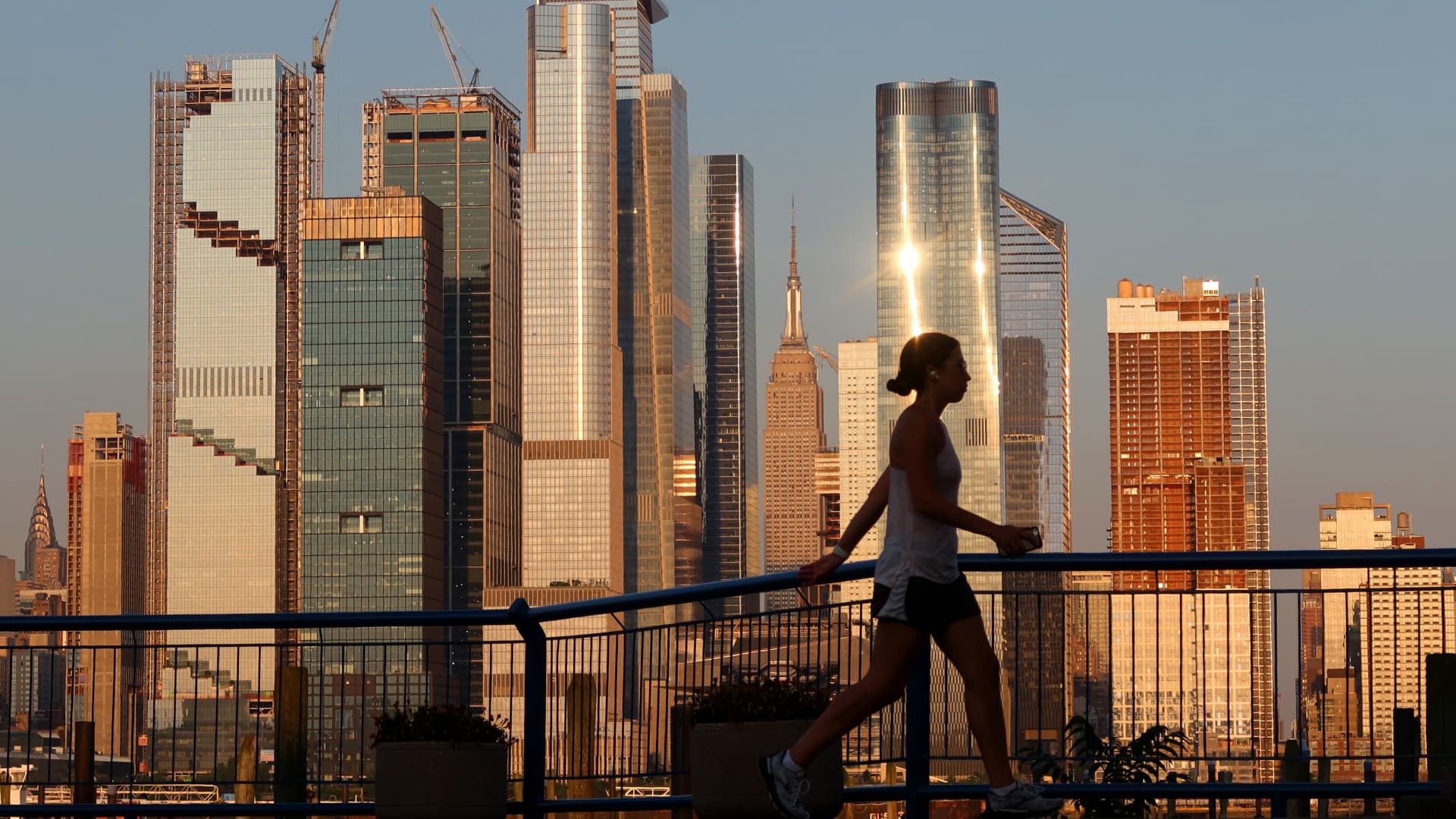 A woman walks past Hudson Yards and the Empire State Building as the sun sets in New York City on June 29, 2021 as seen from Weehawken, New Jersey.