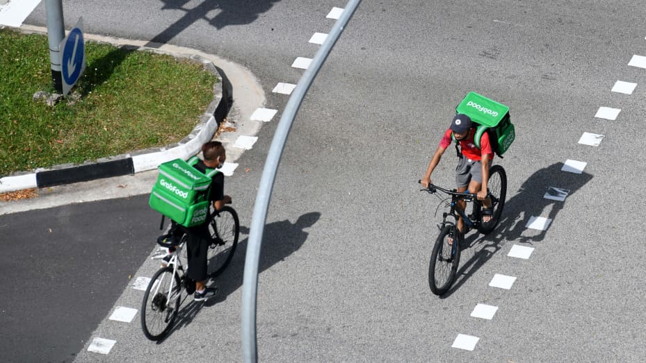 Grab delivery cyclists ride past each other in Singapore on April 20, 2020.