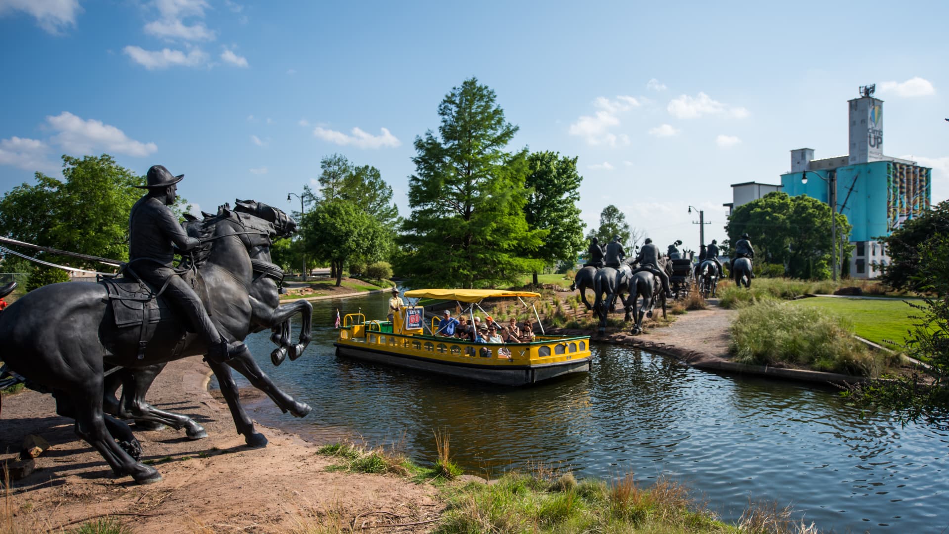 A tourist boat passes cowboy statues along Oklahoma City's Bricktown Canal. Western heritage is a big draw in Oklahoma's capital.
