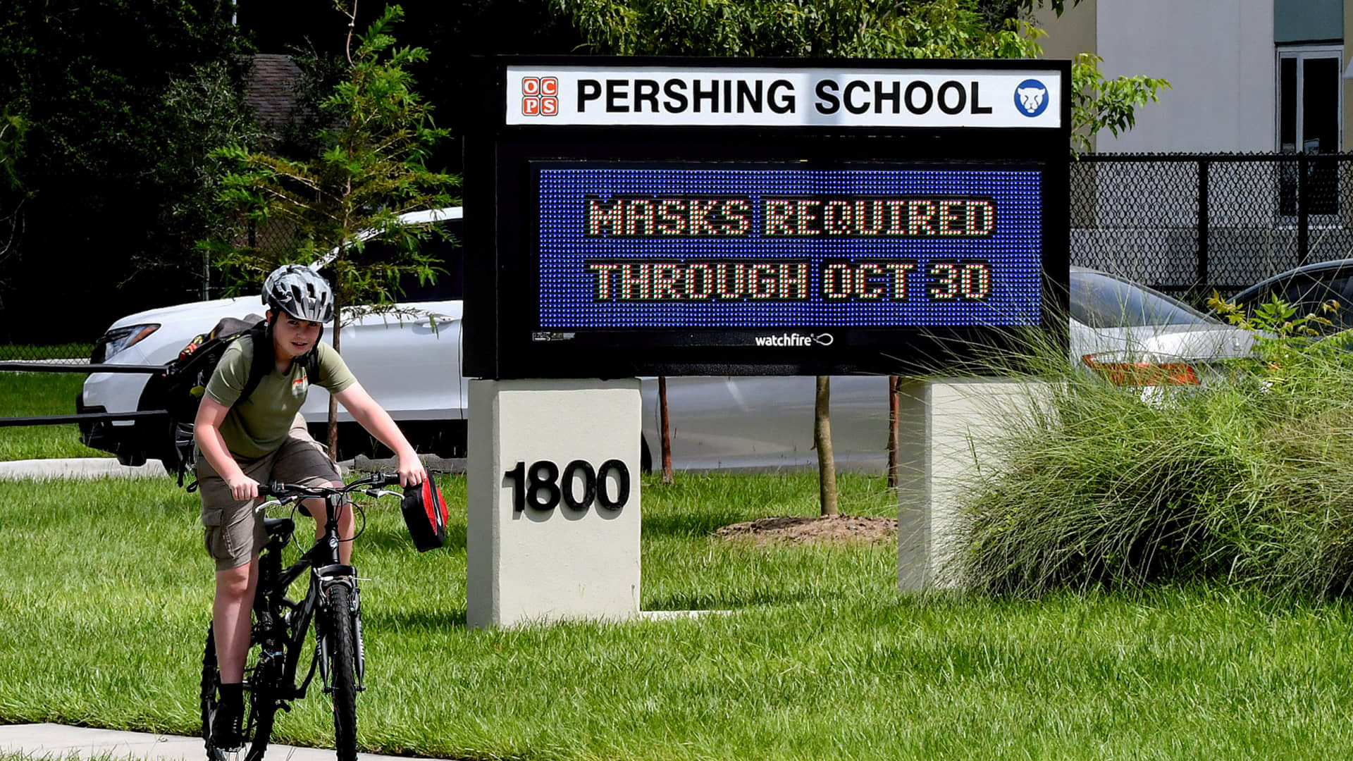 A boy rides a bicycle past a sign at Pershing School in Orlando advising that face masks are required for students through October 30, 2021.