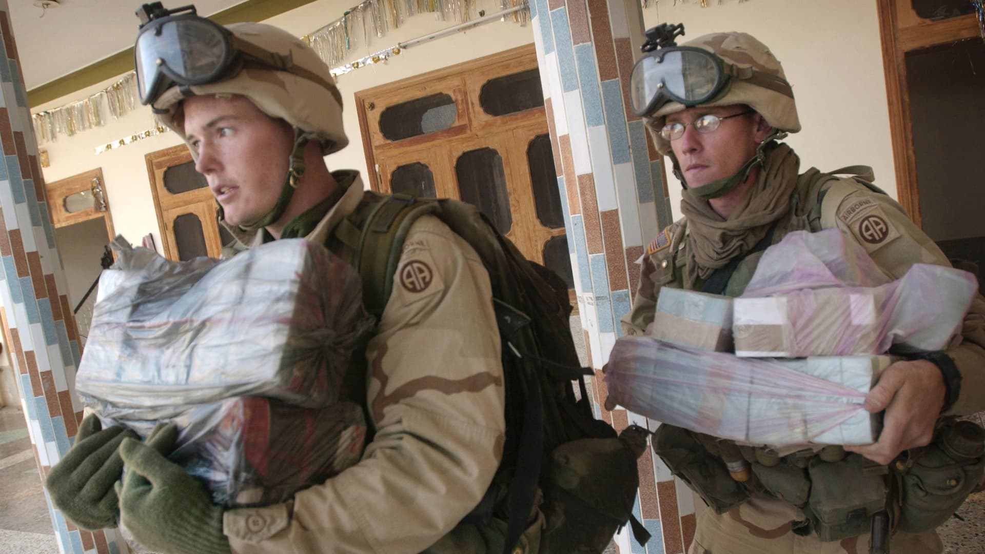 Members of the 82nd Airborne Division carry thousands of dollars in Afghani money found hidden away during an early-morning raid October 1, 2002 in an undisclosed location, in southeastern Afghanistan.