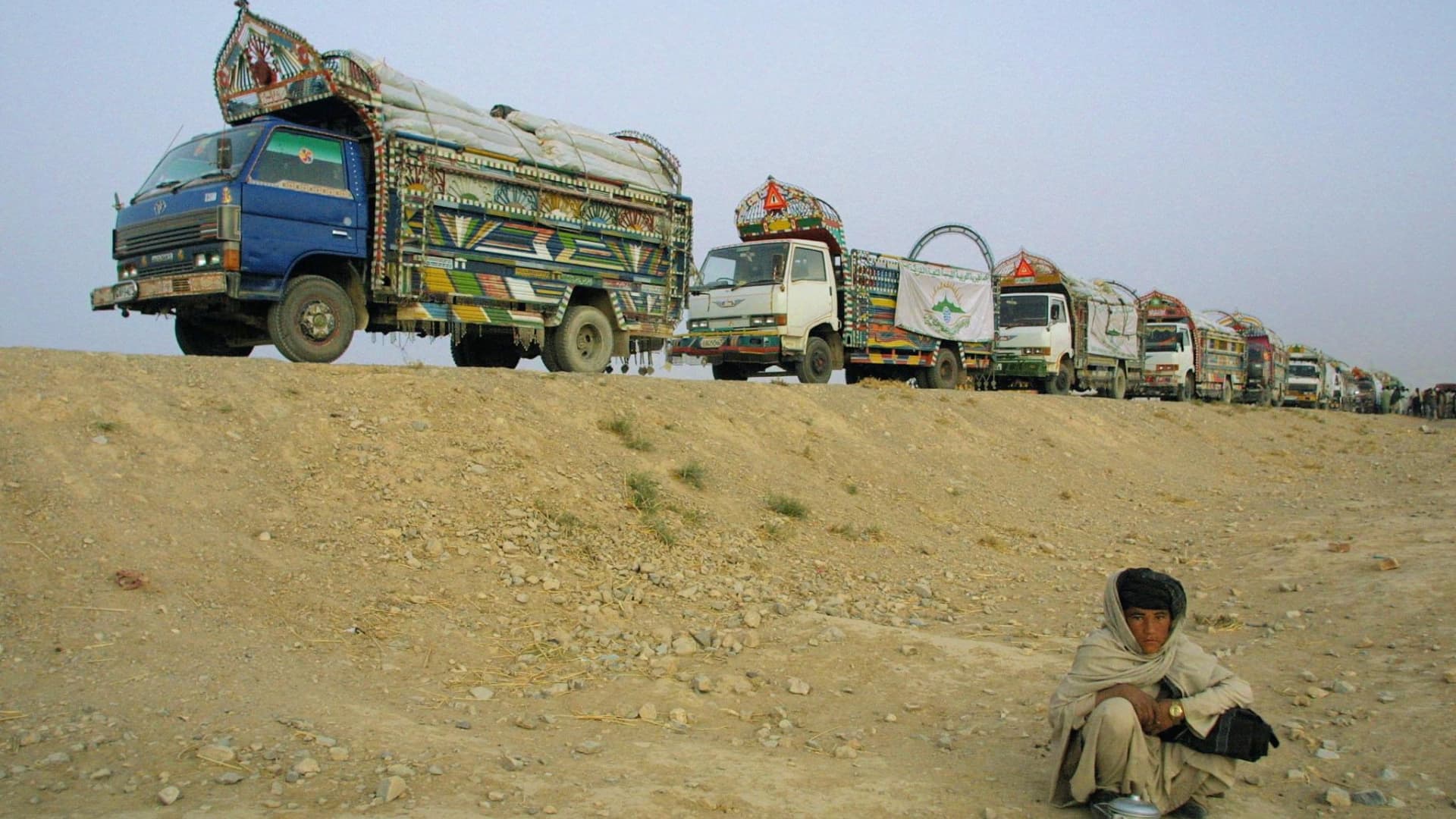 A boy squats near a convoy of 30 trucks parked on the side of a road in Quetta, at dusk 03 November 2001 just before they leave for Kandahar, Afghanistan.