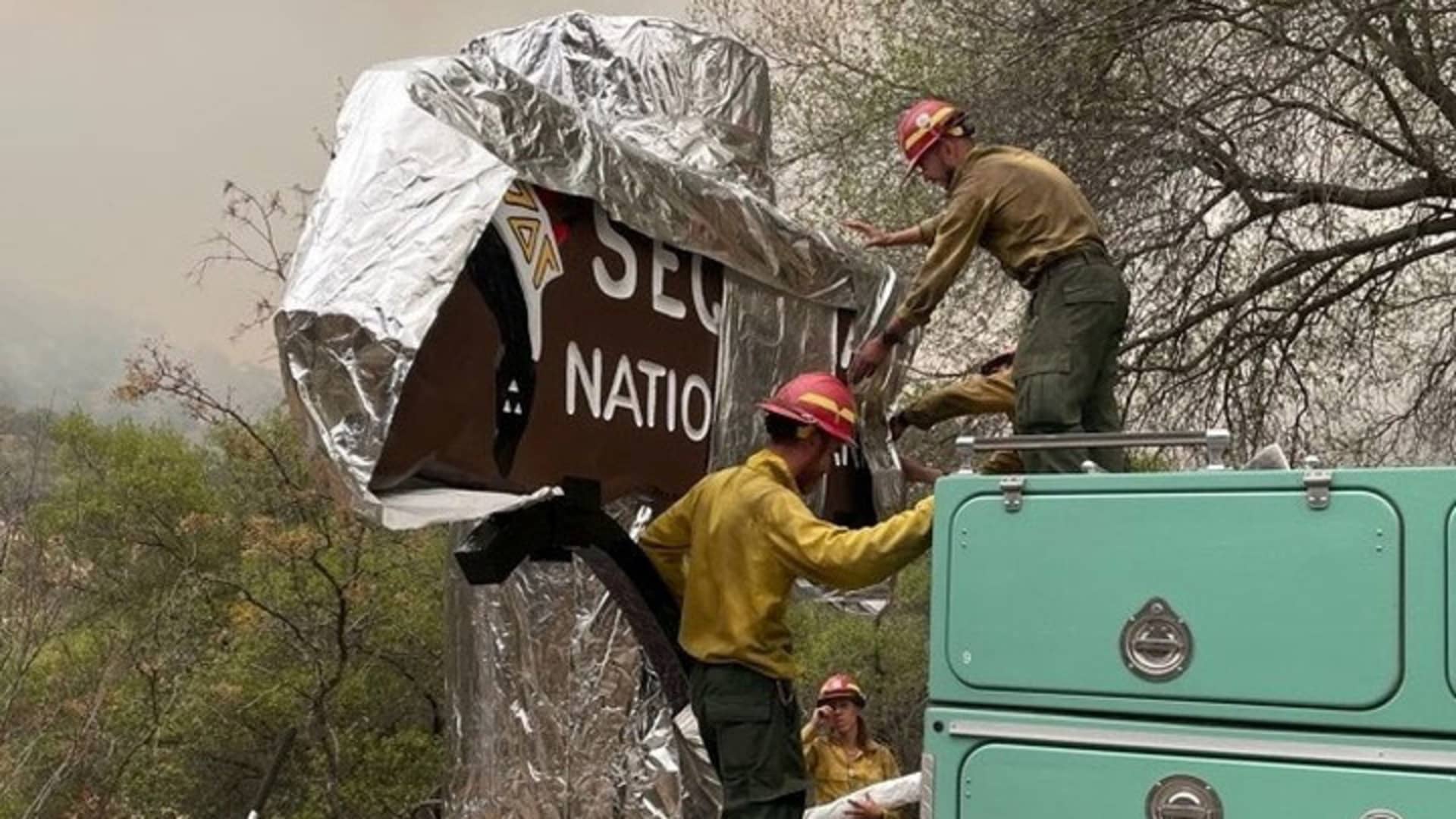 Firefighters cover a sign carved from sequoia wood at an entrance to Sequoia National Park, Sept. 17, 2021.