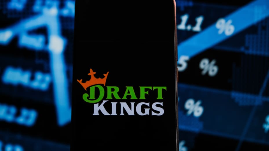 در این تصویر، لوگوی پیش نویس پادشاهان روی گوشی هوشمند با درصدهای بازار سهام در پس‌زمینه نمایش داده می‌شود.