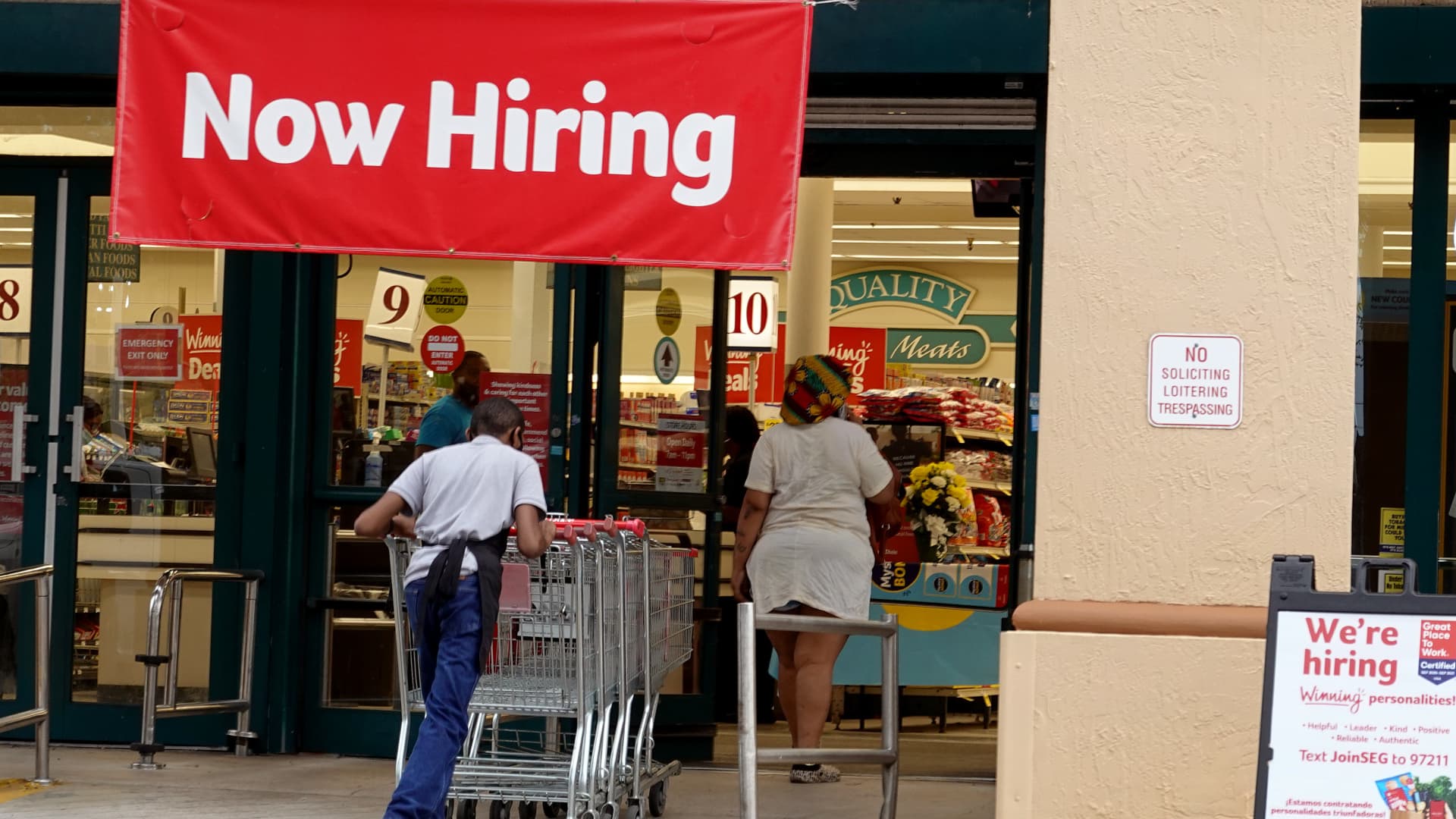A Now Hiring sign hangs near the entrance to a Winn-Dixie Supermarket on September 21, 2021 in Hallandale, Florida.