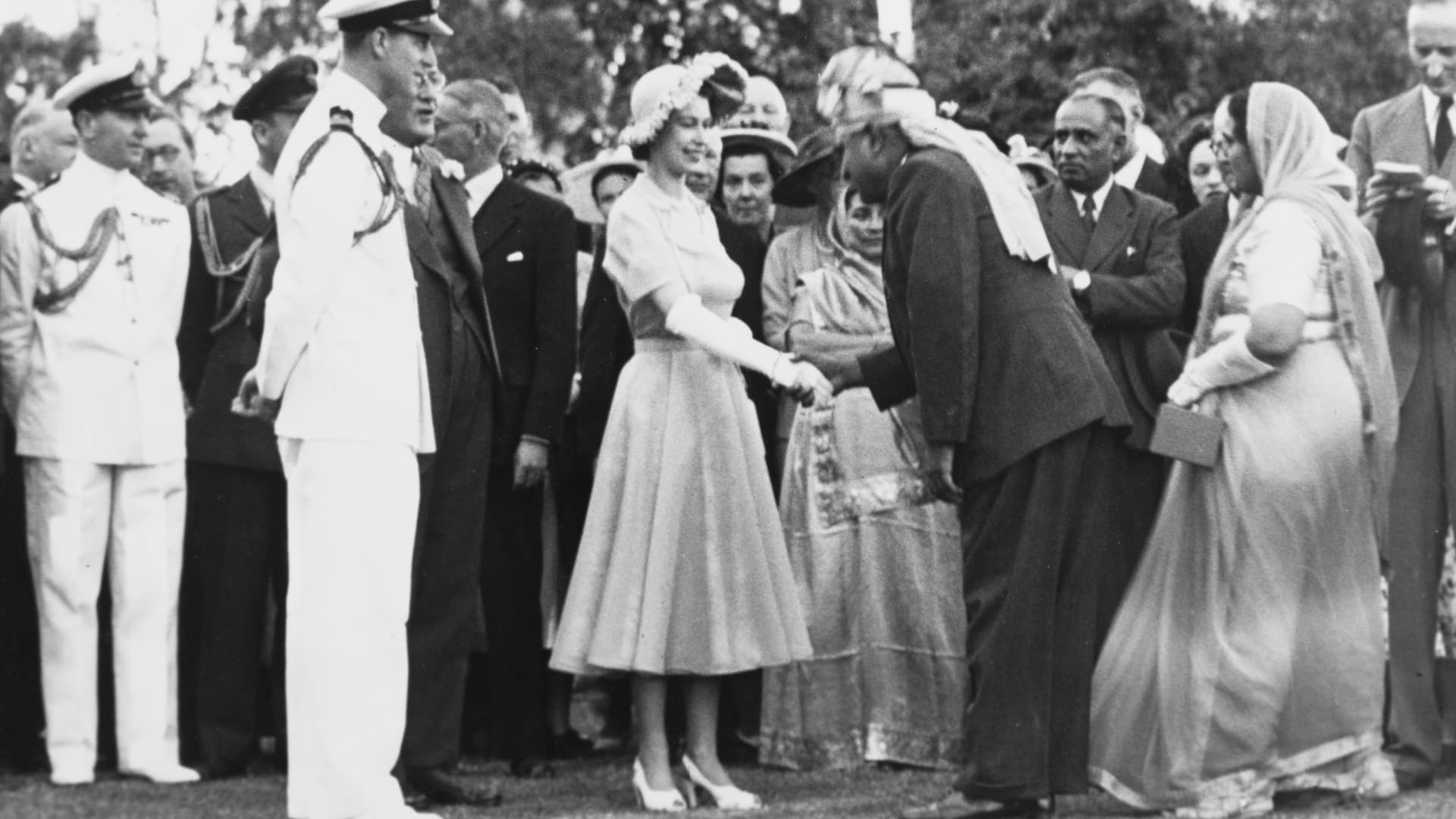 Kenya, Princess Elizabeth and The Duke of Edinburgh are formally greeted by an Asian man who is shaking the Princess's hand. Beside him stands an Asian woman wearing traditional dress.