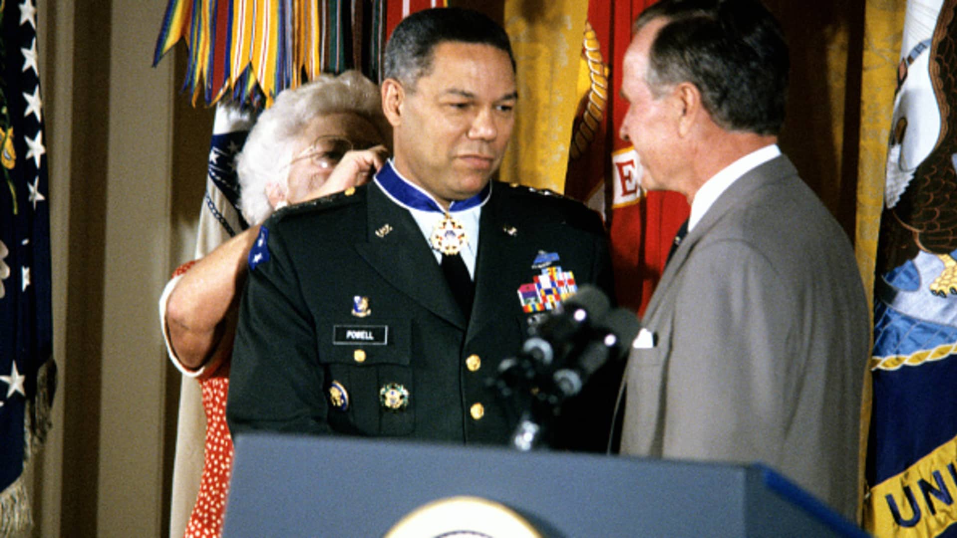 American First Lady Barbara Bush (1925 - 2018) fastens the Presidential Medal of Freedom around the neck of Chairman of the Joint Chiefs of Staff US Army General Colin Powell, as US President George HW Bush (1924 - 2018), watches during a ceremony in the White House's East Room, Washington DC, July 3, 1991.