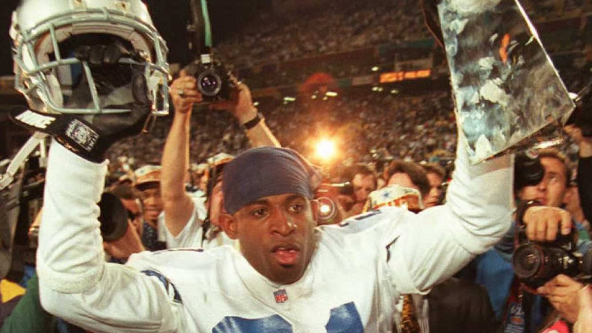 Dallas Cowboys cornerback Deion Sanders hoists the Vince Lombardi Super Bowl trophy as he walks off the field to the locker room after defeating the Pittsburgh Steelers 28 January during Super Bowl XXX at Sun Devil Stadium in Tempe, Arizona. The Cowboys won 27-17.