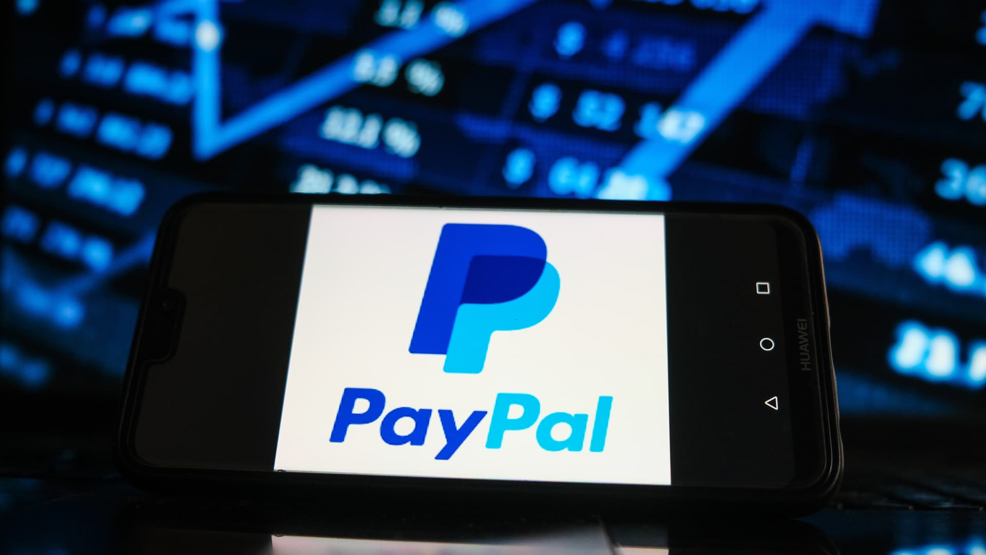 The PayPal logo displayed on a smartphone screen with a stock market graphic in the background.