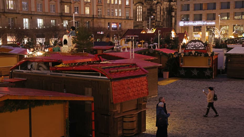 People walk among closed stands that would normally be selling gluehwein, stollen bread, Christmas tree decorations and other Christmas delights at the shuttered Striezelmarkt Christmas market during the fourth wave of the coronavirus pandemic on November 23, 2021 in Dresden, Germany.