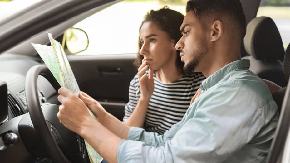 Puzzled middle-eastern young couple sitting in automobile, watching map, side view. Millennial travellers having car trip, got lost on the road, looking for way to destination point, closeup