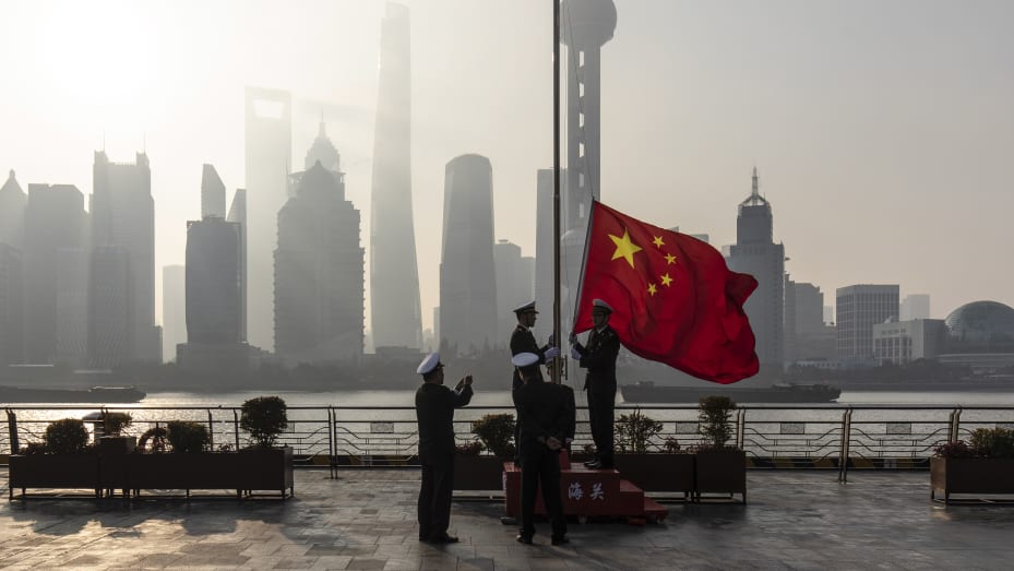 China customs officers raise a Chinese flag during a rehearsal for a flag-raising ceremony along the Bund in front of buildings in the Lujiazui Financial District at sunrise in Shanghai, China, on Tuesday, Jan. 4, 2022.