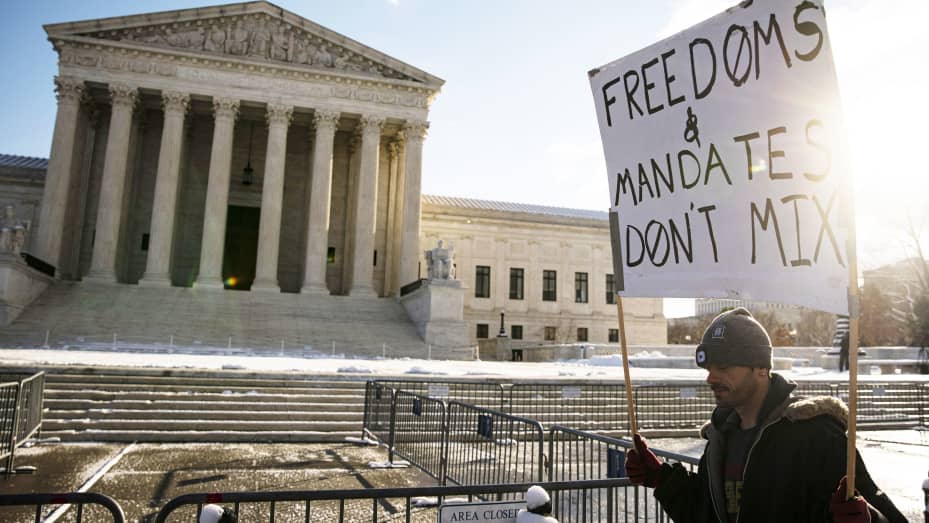 A demonstrator holds a "Freedoms & Mandates Don't Mix" sign outside the U.S. Supreme Court during arguments on two federal coronavirus vaccine mandate measures in Washington, D.C., U.S., on Friday, Jan. 7, 2022.