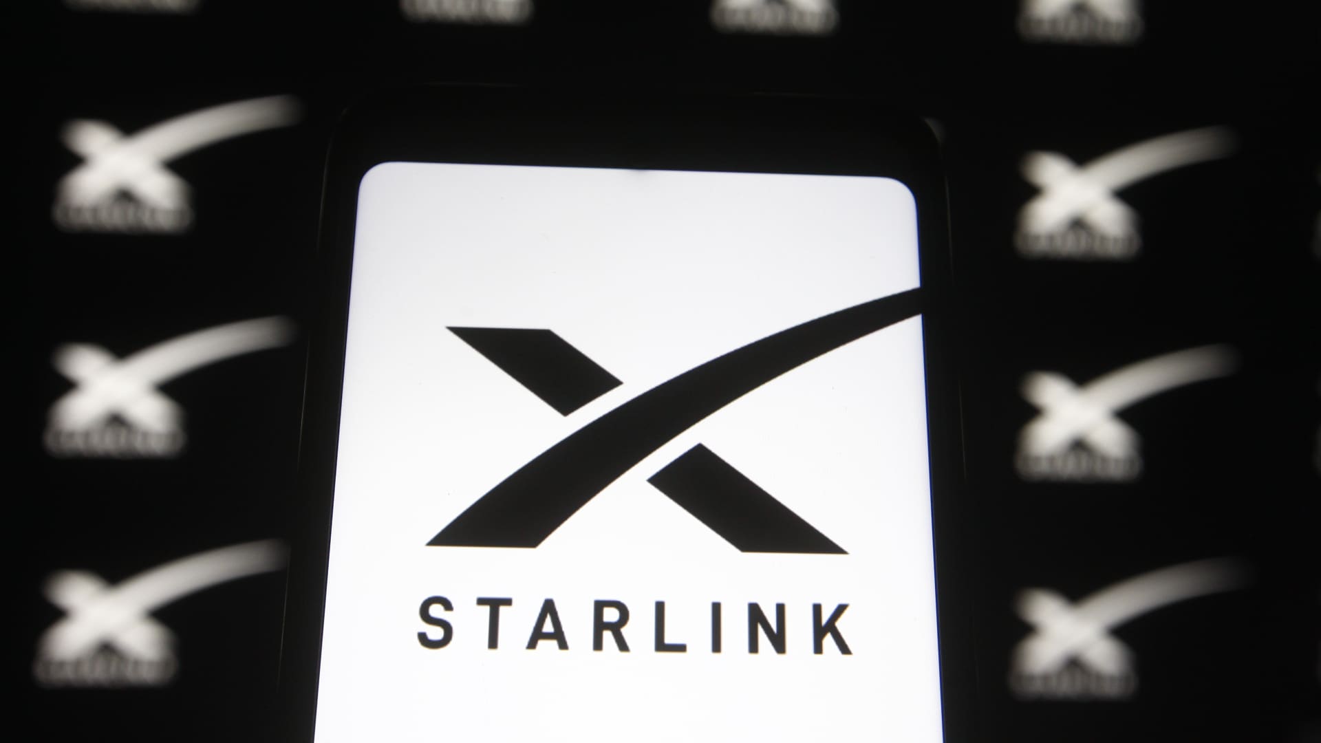A Starlink logo of a satellite internet constellation being constructed by SpaceX is seen on a smartphone and a pc screen.