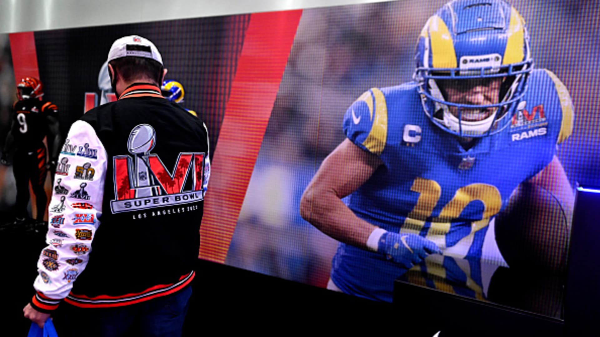 A fan wearing a super boal jacket walks past a giant picture of Los Angeles Rams Cooper Kupp during the Super Bowl Experience at the Los Angeles Convention Center in Los Angeles on Saturday, February 5, 2022.