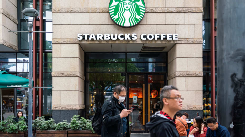 Pedestrians wearing face masks walk past an American coffee company and coffeehouse chain Starbucks store in Shanghai.