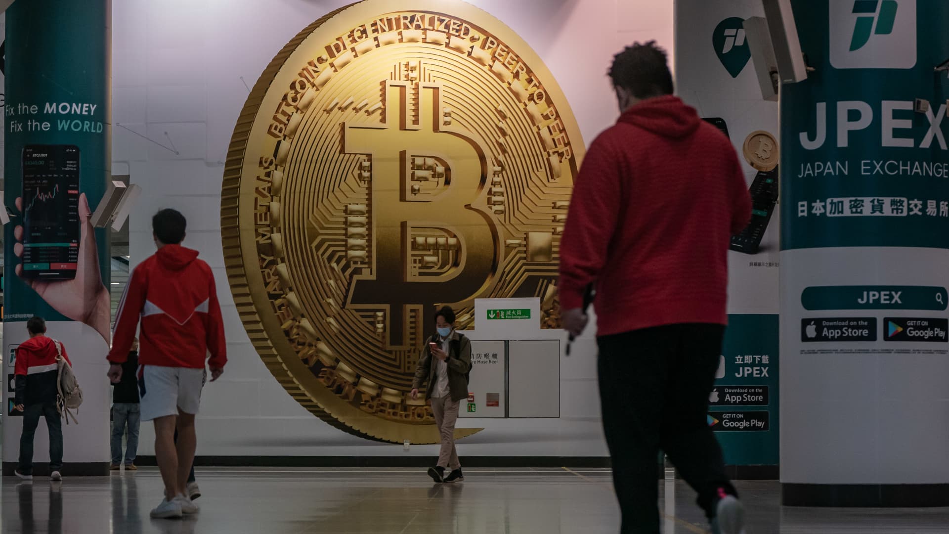 Pedestrians walk past an advertisement displaying a Bitcoin cryptocurrency token on February 15, 2022 in Hong Kong, China.