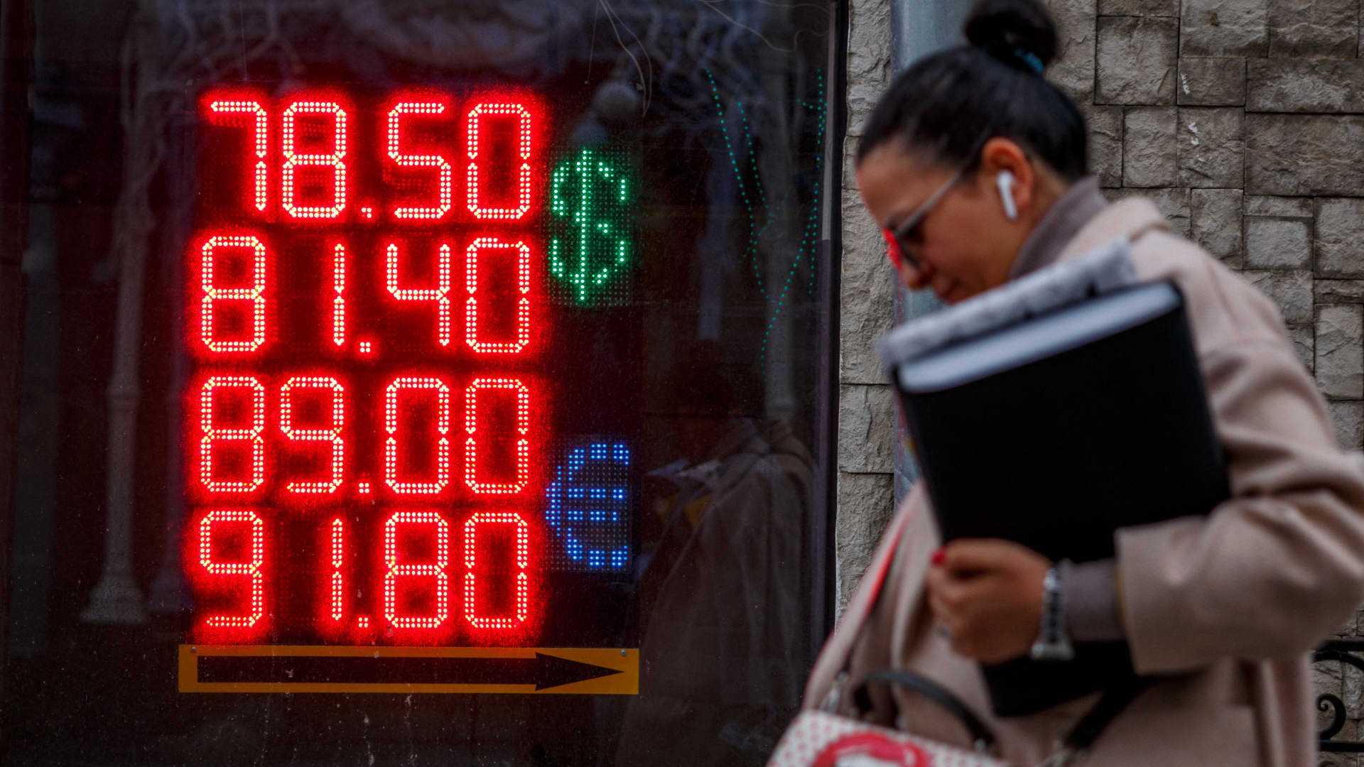 A woman walks past a board showing currency exchange rates of the US dollar and the euro against Russian ruble in Moscow on February 22, 2022.