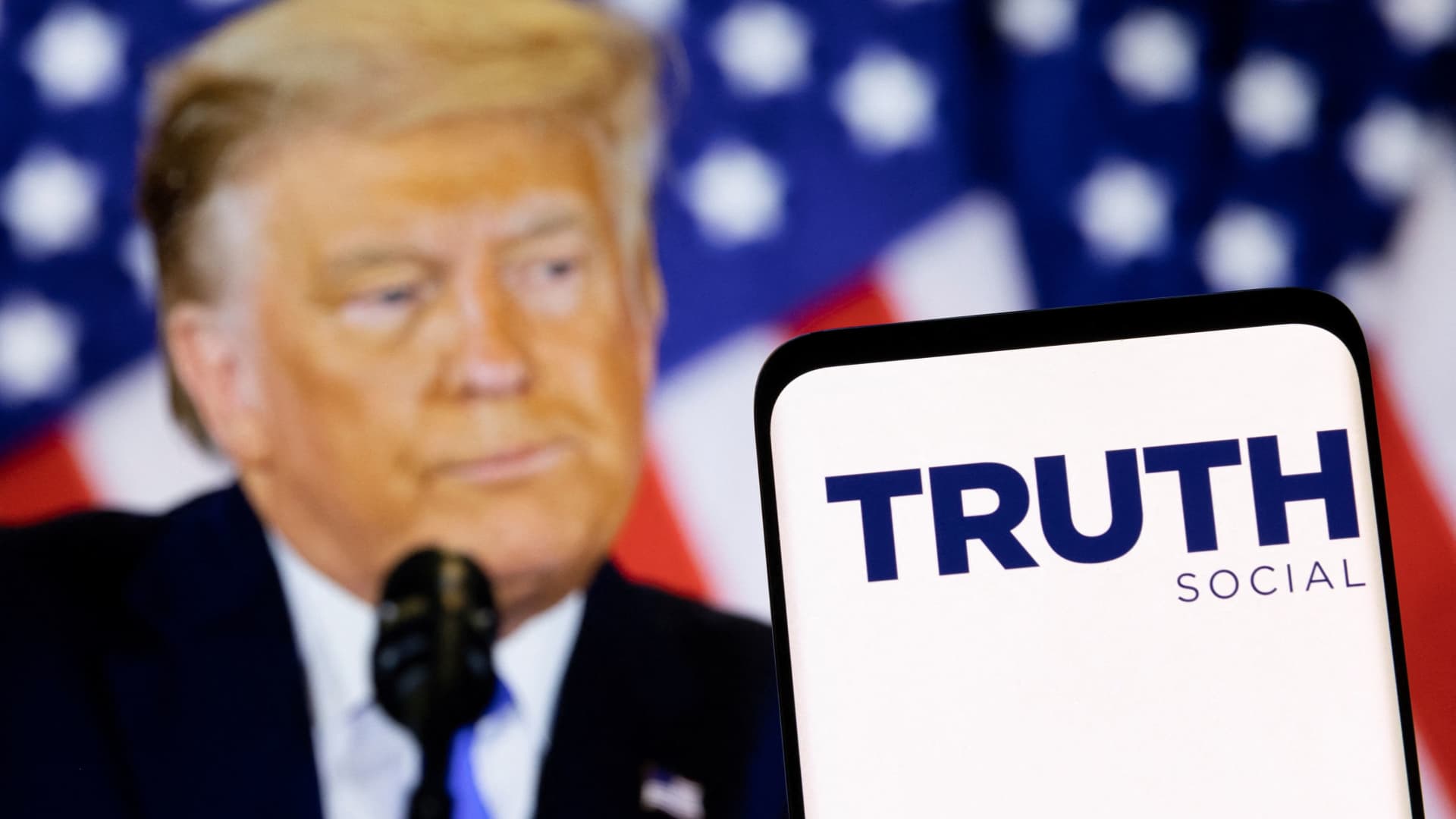 The Truth social network logo is seen on a smartphone in front of a display of former U.S. President Donald Trump in this picture illustration taken February 21, 2022.