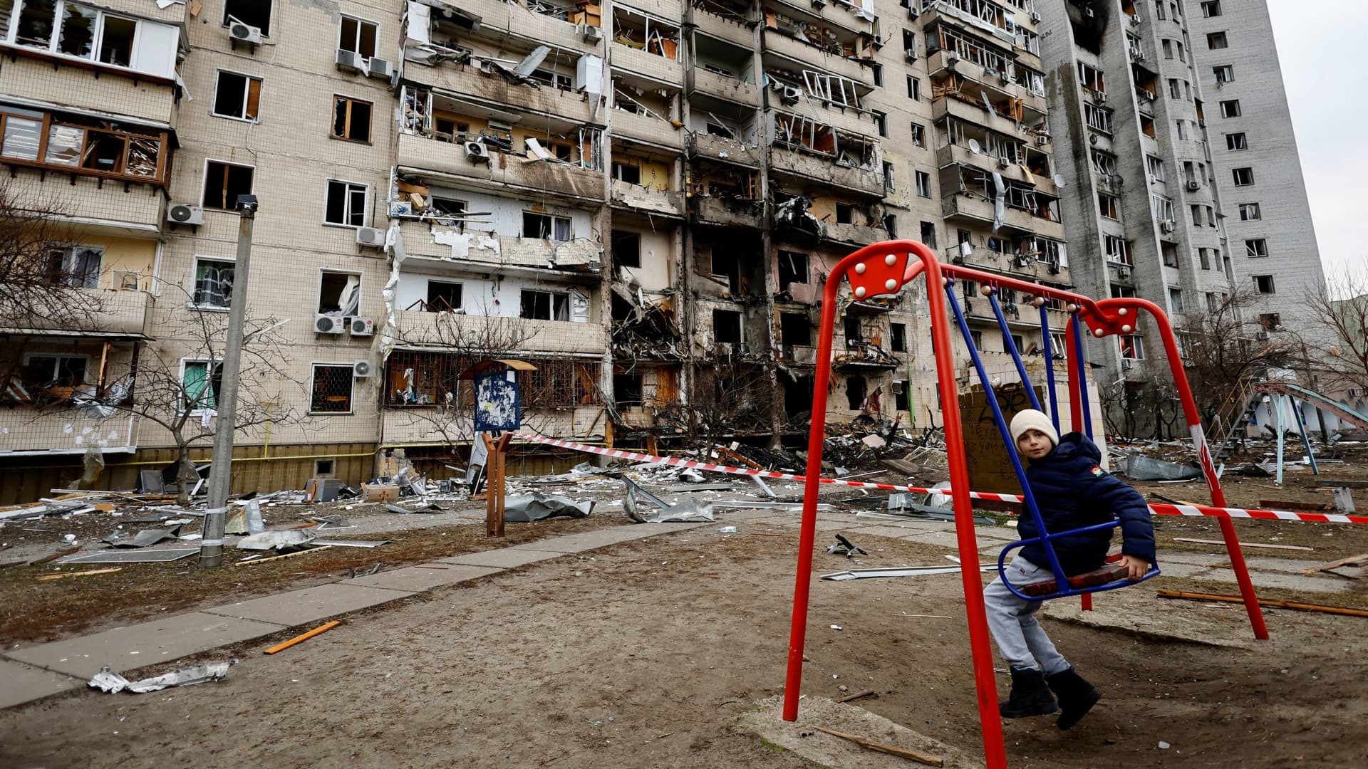 A child sits on a swing in front of a damaged residential building, after Russia launched a massive military operation against Ukraine, in Kyiv, Ukraine February 25, 2022.