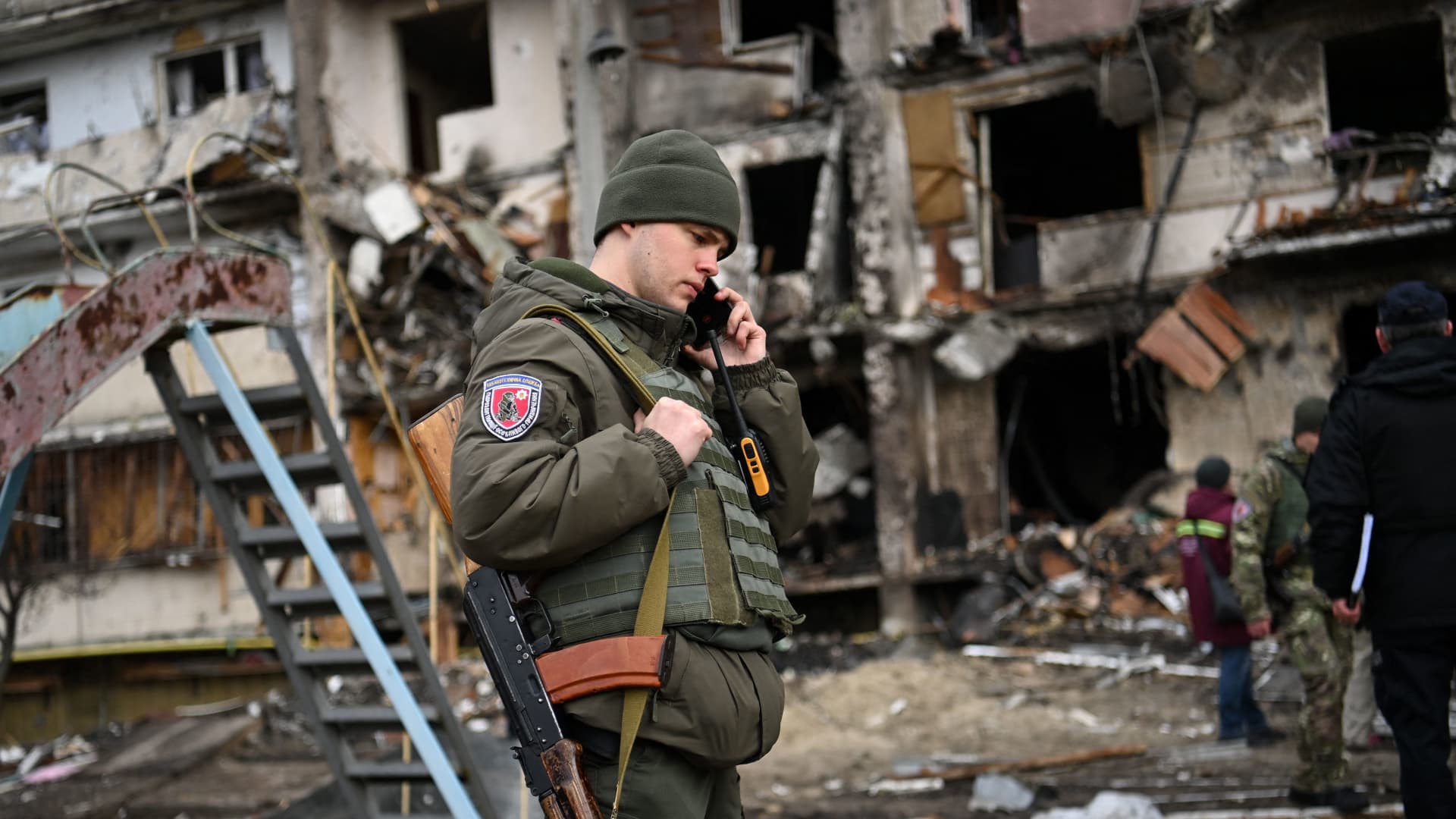 A Ukrainian serviceman talks on a smartphone in front of a damaged residential building at Koshytsa Street, a suburb of the Ukrainian capital Kyiv, where a military shell allegedly hit, on February 25, 2022.