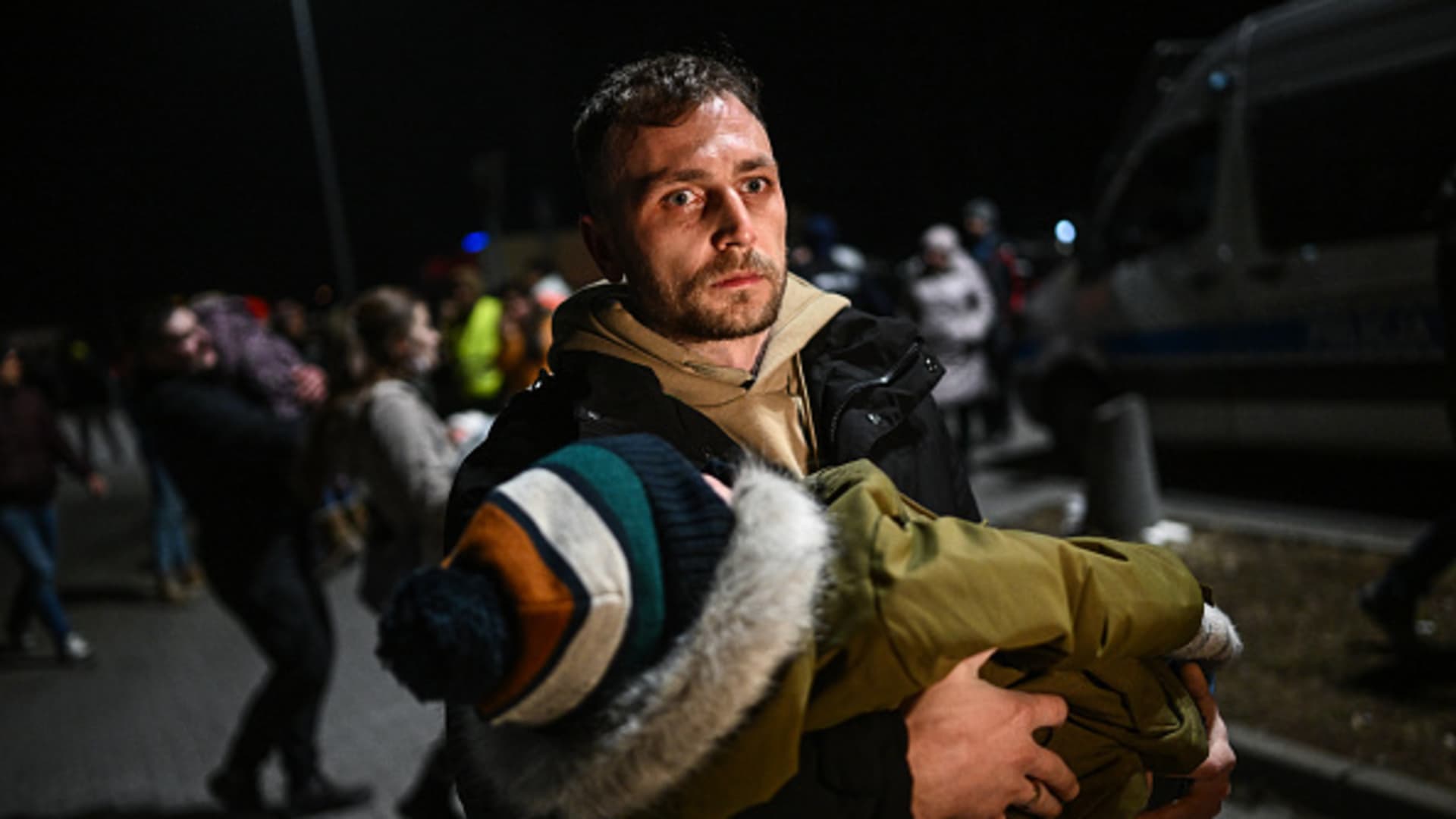 A man holds a sleeping baby after arriving by bus to a supermarket parking lot from the Polish-Ukrainian border crossing on February 25, 2022 in Przemysl, Poland.