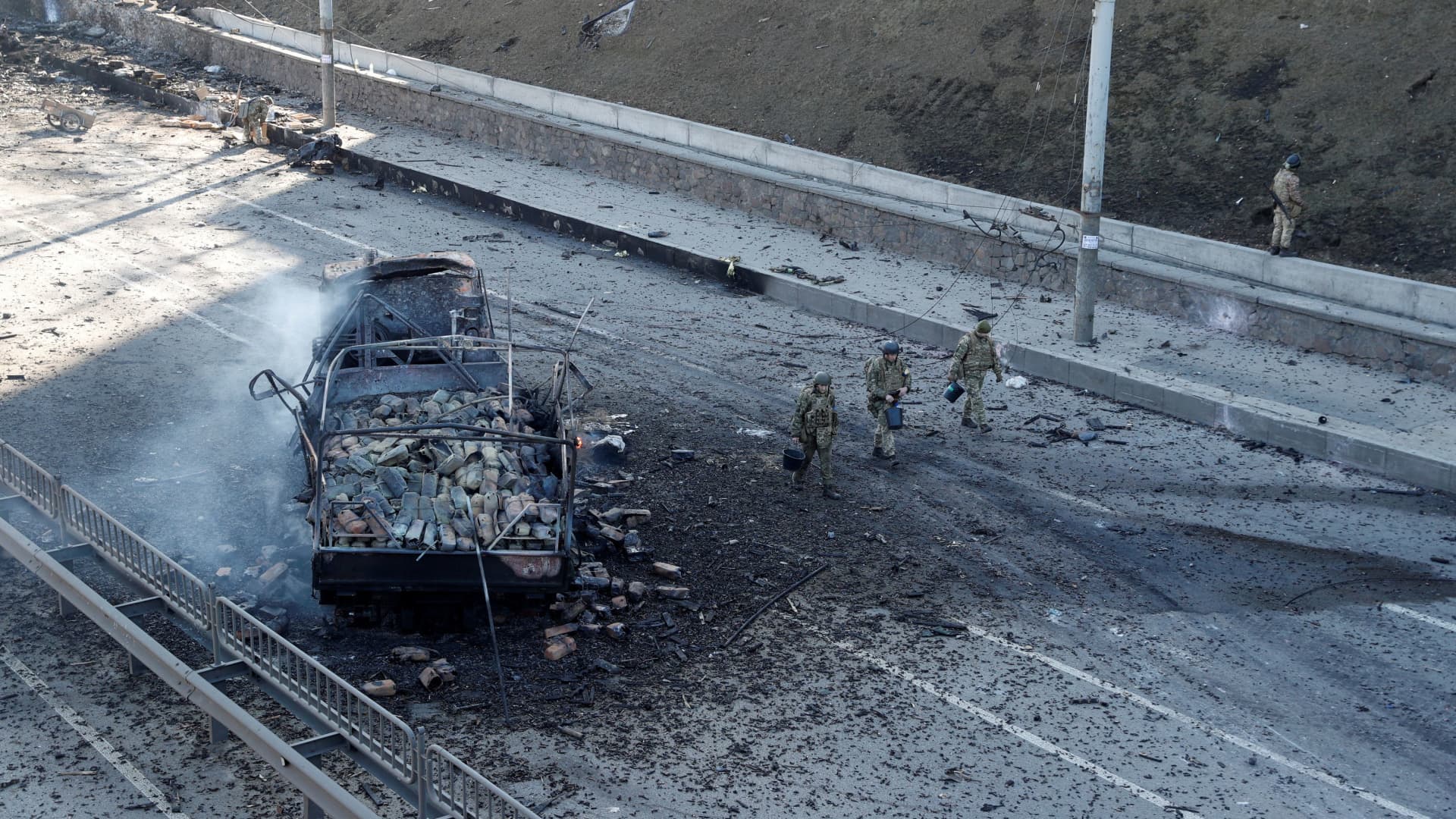 Ukrainian servicemen walk by a damaged vehicle, at the site of a fighting with Russian troops, after Russia launched a massive military operation against Ukraine, in Kyiv, Ukraine February 26, 2022.