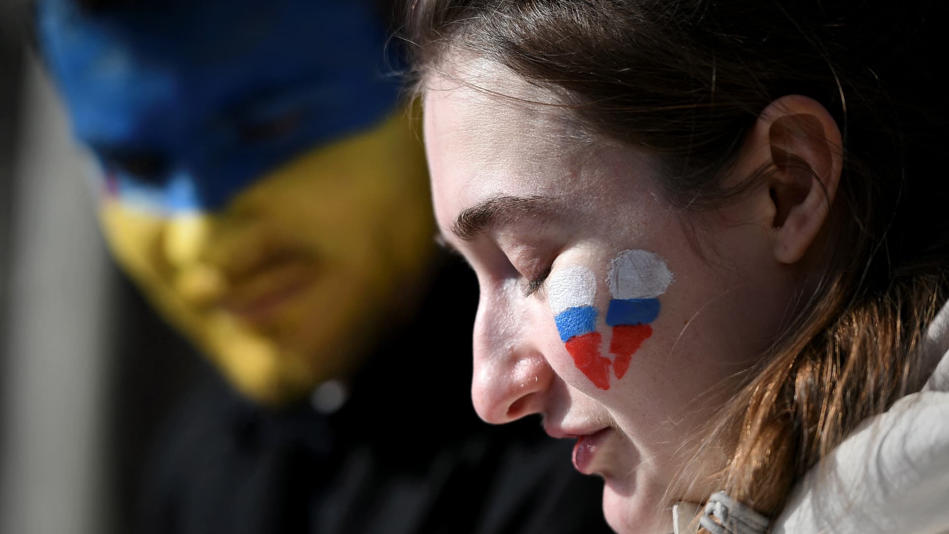 A men with blue and yellow make-up on his face, colours of the Ukrainian flag, and a woman with a broken heart in the colours of the Russian flag make-up on her face attend a demonstration at the Place du Capitole, in Toulouse, southern France, on February 27, 2022, against the Russian invasion in Ukraine.