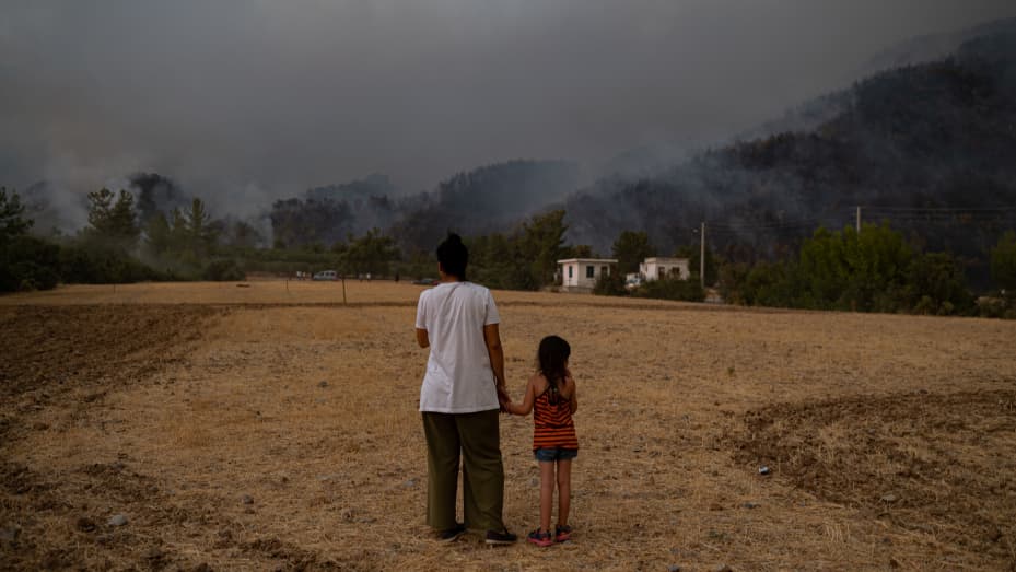 TOPSHOT - A woman and child stand in a field as they watch wildfires as they burn in Koycegiz district of Mugla on August 3, 2021. - Turkey's struggles against its deadliest wildfires in decades come as a blistering heatwave grips southeastern Europe crea