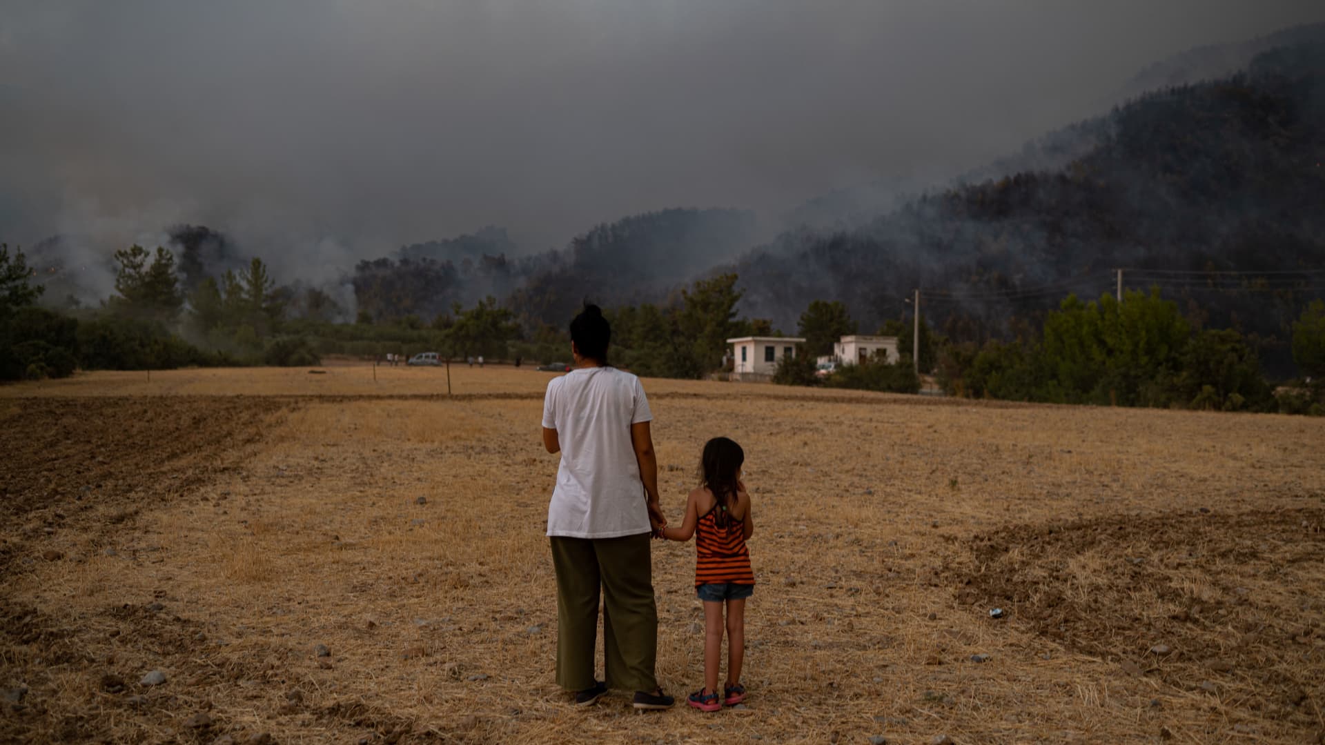 TOPSHOT - A woman and child stand in a field as they watch wildfires as they burn in Koycegiz district of Mugla on August 3, 2021.