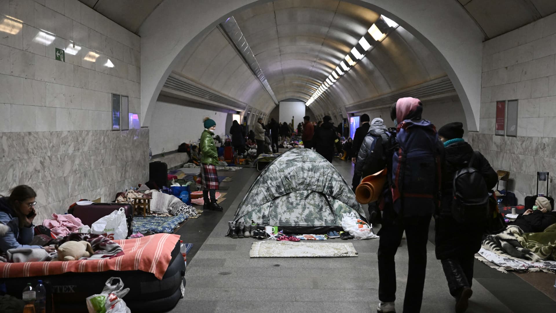 Civilians walk by Ukraine residents who use an underground metro station as bomb shelter in Kyiv on March 2, 2022.