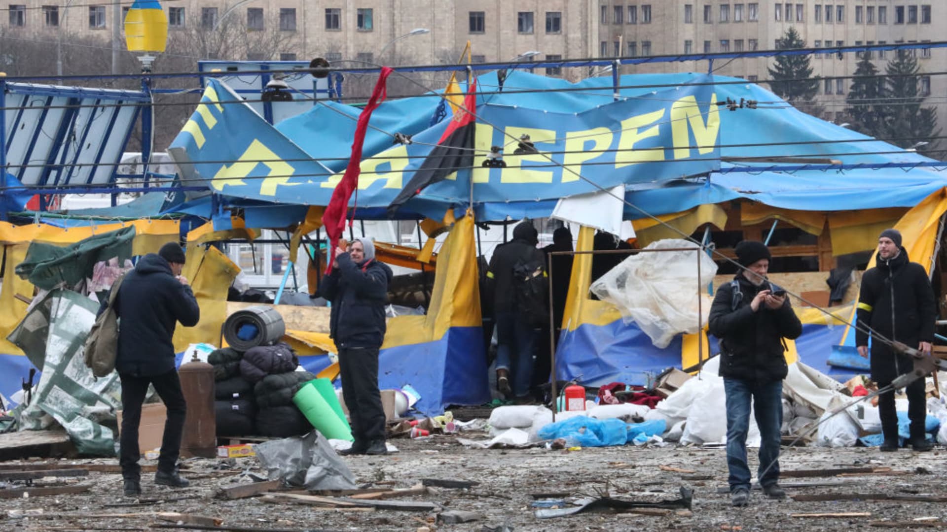 People stay by the All for Victory Tent of volunteers after a missile launched by Russian invaders hit outside the Kharkiv Regional State Administration building in SvobodySquare at approximately 8 am local time on Tuesday, March 1, Kharkiv, northeastern Ukraine.