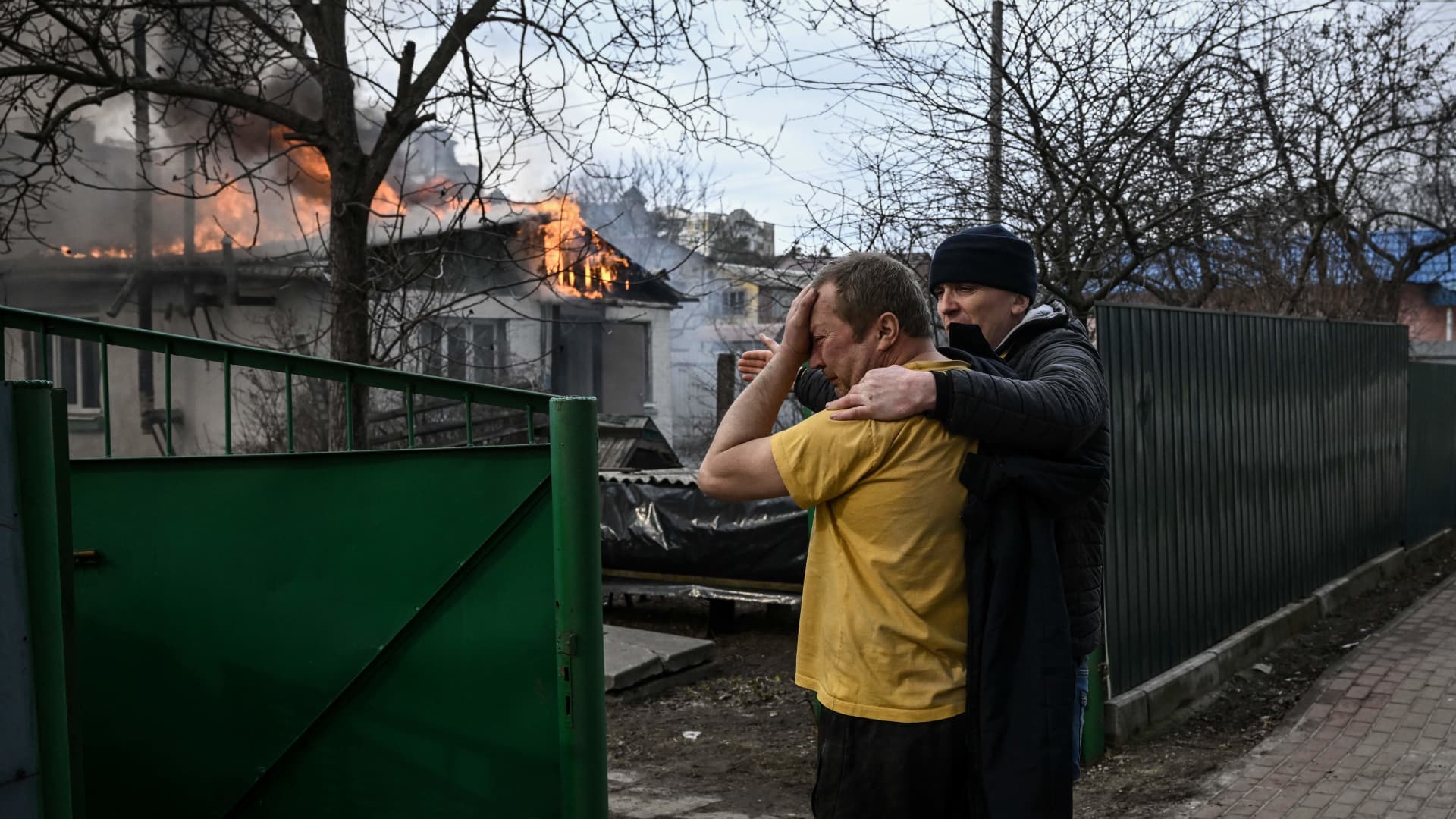 Yevghen Zbormyrsky, 49, is comfirted as he stands in front of his burning home after it was hit by a shelled in the city of Irpin, outside Kyiv, on March 4, 2022. 