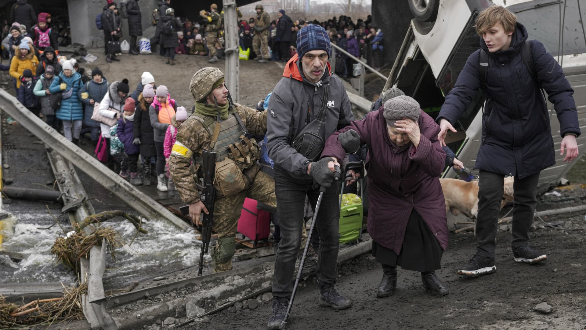 An elderly lady is assisted while crossing the Irpin river, under a bridge that was destroyed by a Russian airstrike, as civilians flee the town of Irpin, Ukraine, Saturday, March 5, 2022.